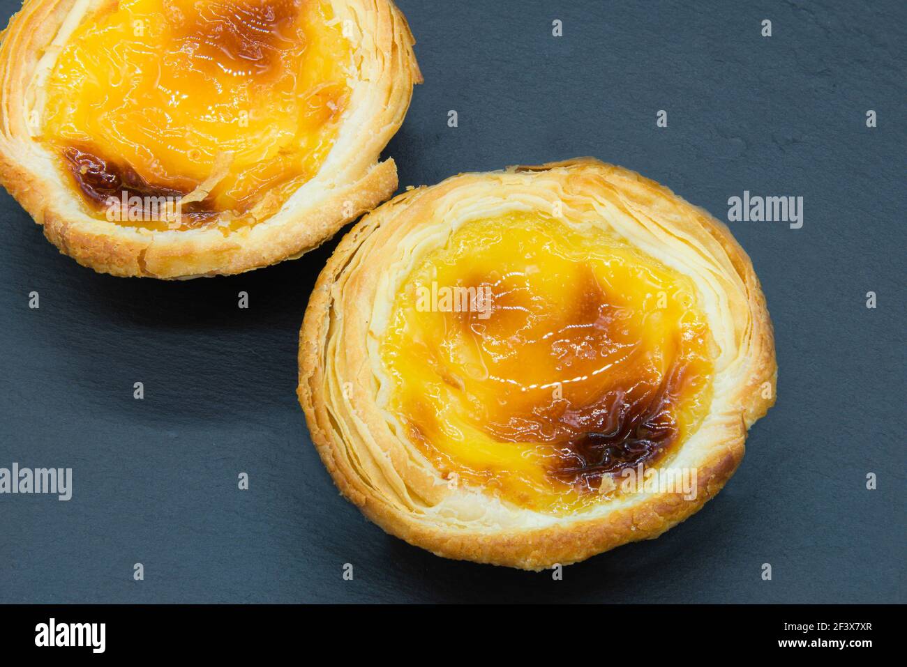 Deux petites tartes de crème anglaise sur un fond gris foncé. Banque D'Images