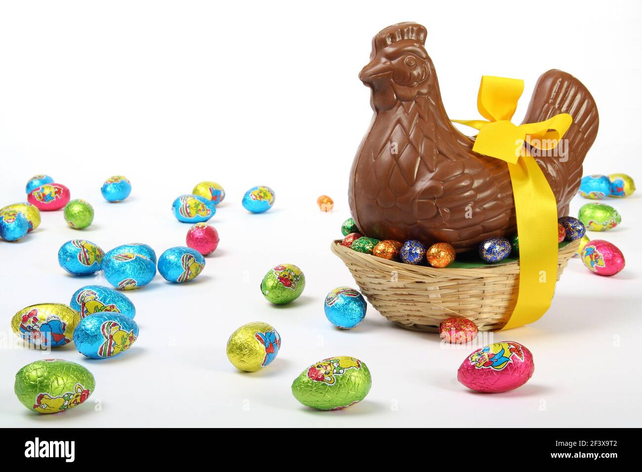 Poule de Pâques au chocolat avec ruban jaune et noeud, présenté avec des oeufs décoratifs colorés, isolés sur fond blanc Banque D'Images