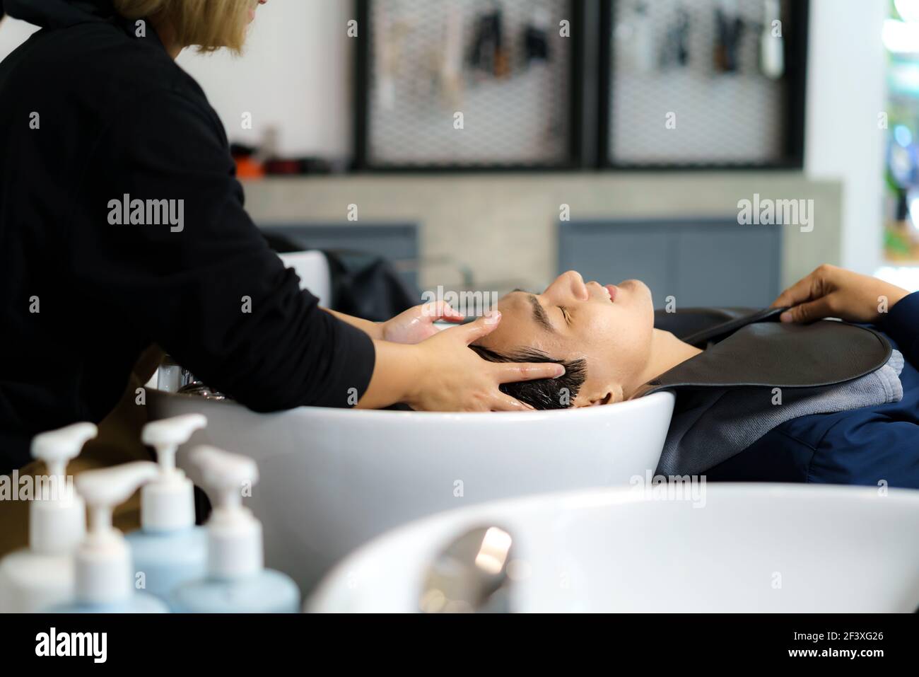 Coiffeur applique le shampooing et massant les cheveux d'un client. Homme ayant ses cheveux lavés dans un salon de coiffure. Banque D'Images