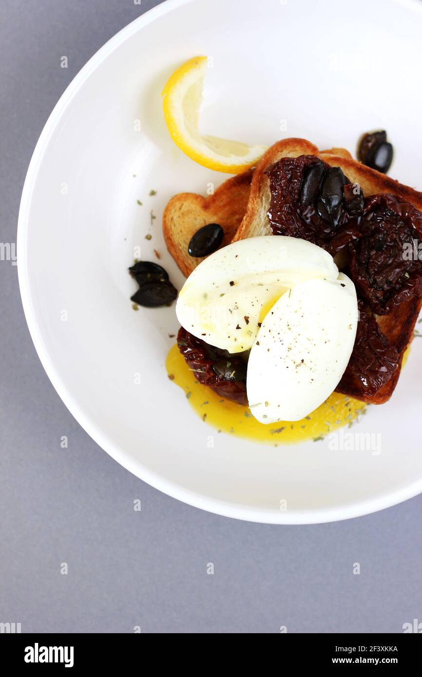 Petit déjeuner, brunch. Œuf poché avec jaune d'œuf liquide, tomates séchées avec graines sur toasts. Banque D'Images