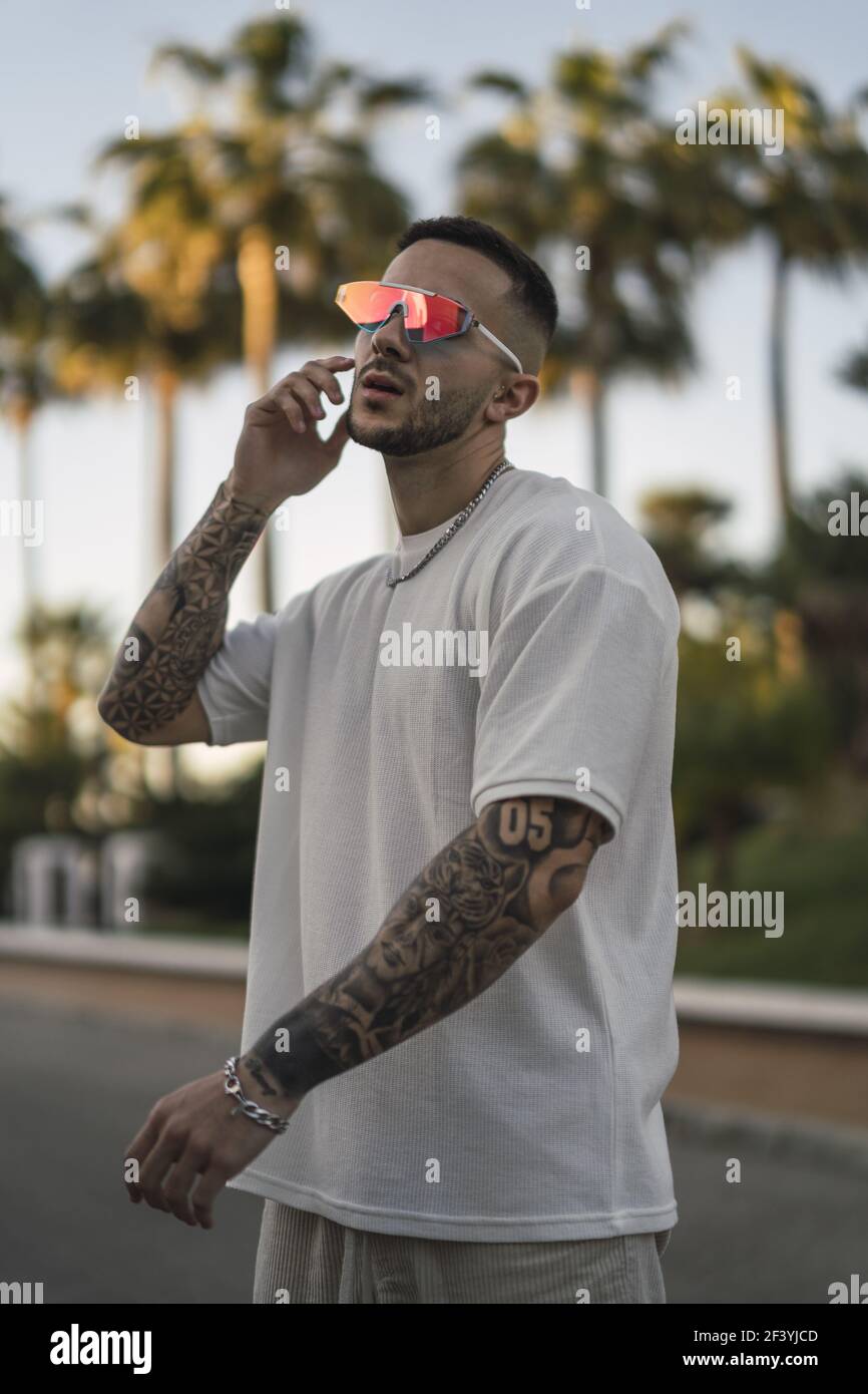 Un cliché vertical d'un beau homme espagnol de race blanche tatouages et lunettes  de soleil posant à l'extérieur Photo Stock - Alamy