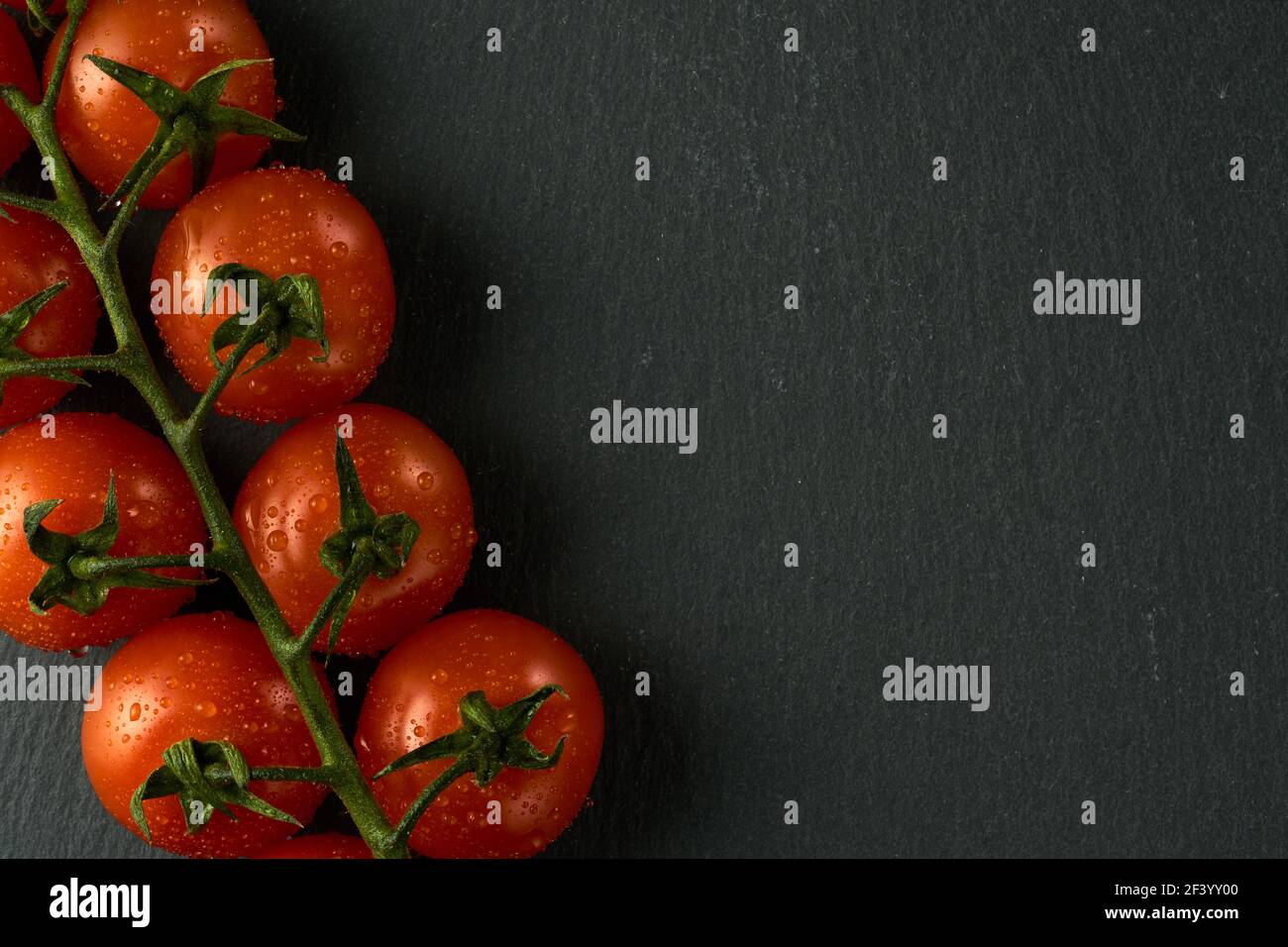 Tomates cerises sur une table en pierre noire. L'image peut également être utilisée comme texture, j'ai laissé un espace pour le texte sur le côté droit. Banque D'Images