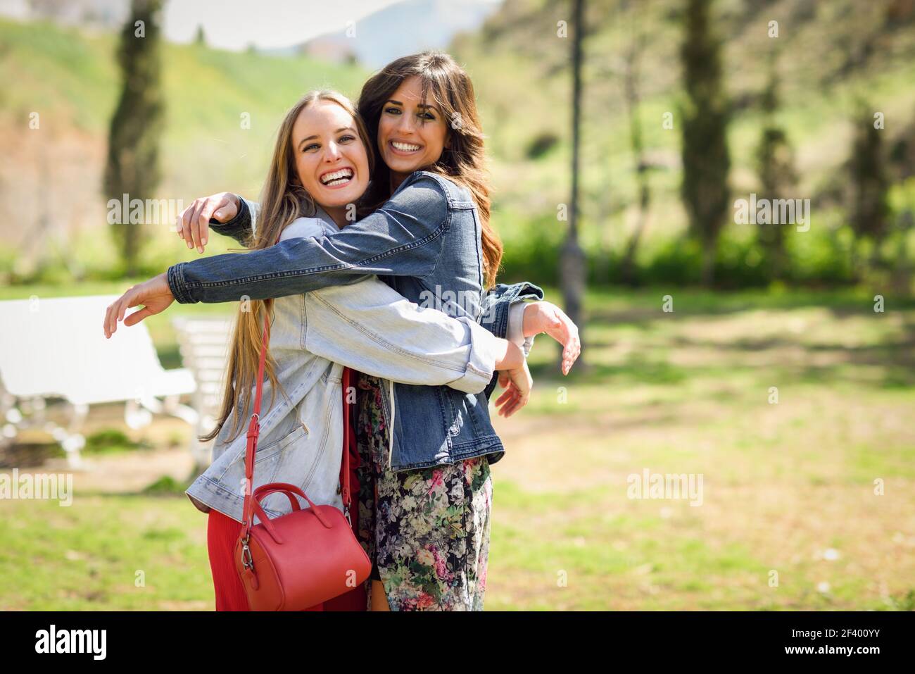 Deux filles heureux hugging in parc urbain. Blonde et brunette filles portant des vêtements à l'extérieur. Banque D'Images