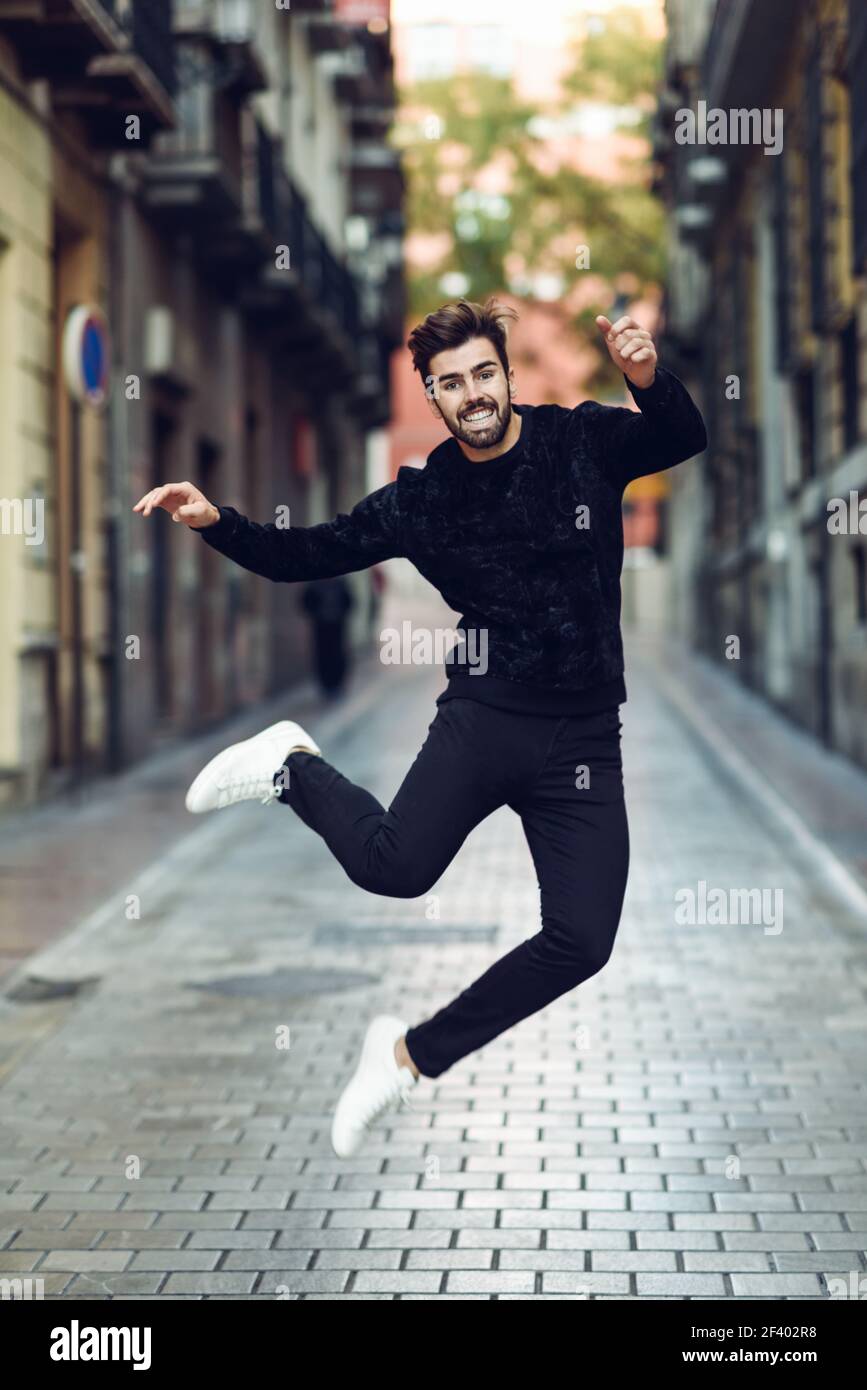 Jeune homme barbu qui saute dans les rues portant des vêtements décontractés. Heureux guy avec barbe et coiffure moderne. Banque D'Images