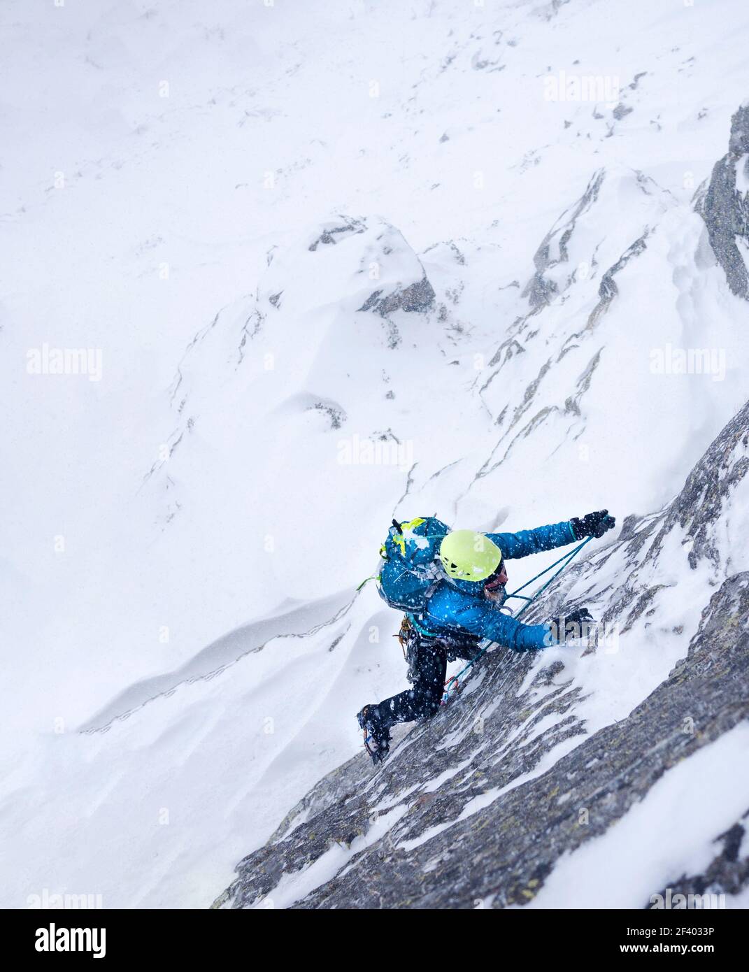 Femme grimpant dans la tempête lors d'une ascension hivernale extrême. Alpes italiennes de l'Ouest, Europe. Banque D'Images