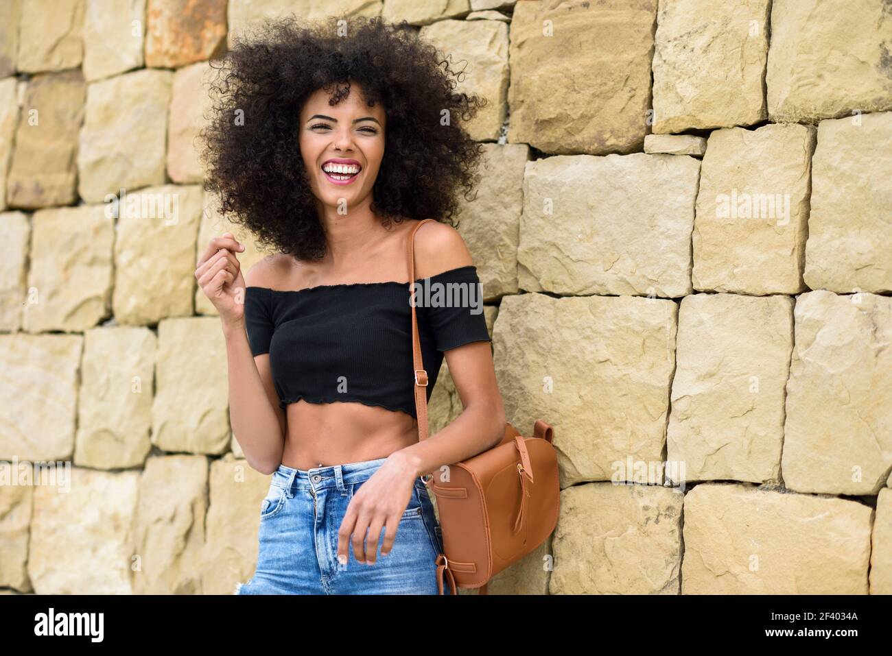 Happy mixed femme avec cheveux afro de rire à l'extérieur. Femme portant des vêtements décontractés en contexte urbain. Concept de vie Banque D'Images
