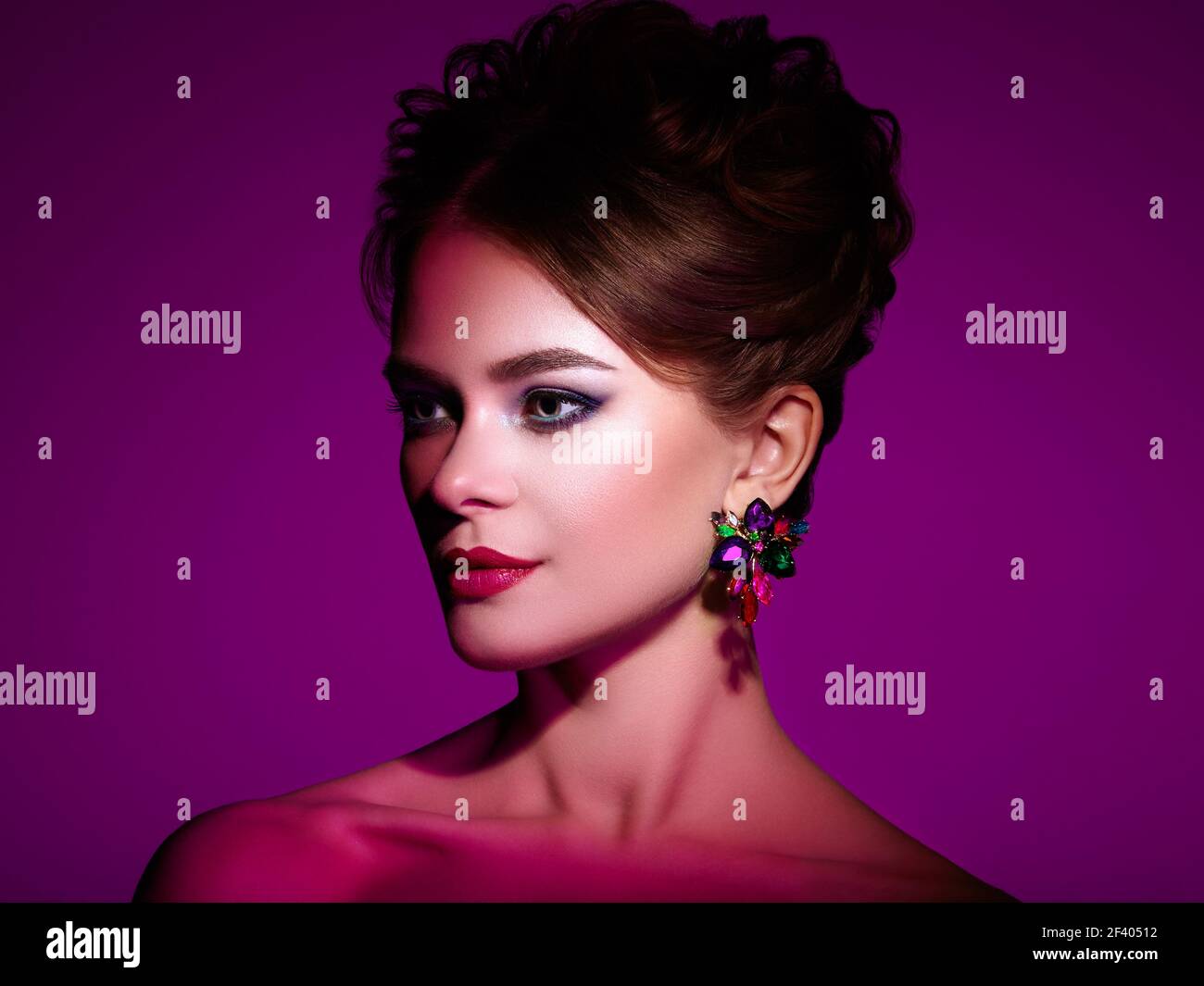 Brunette Girl avec une élégante coiffure de curly. Belle femme modèle avec de beaux boucles d'oreilles précieuses. Produits de soins et de beauté pour cheveux. Maquillage et bijoux parfaits. Arrière-plan violet spectaculaire Banque D'Images