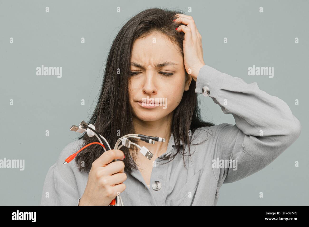 Photo d'une femme mignonne déçue des chargeurs cassés. Porte une robe grise, un fond gris isolé Banque D'Images