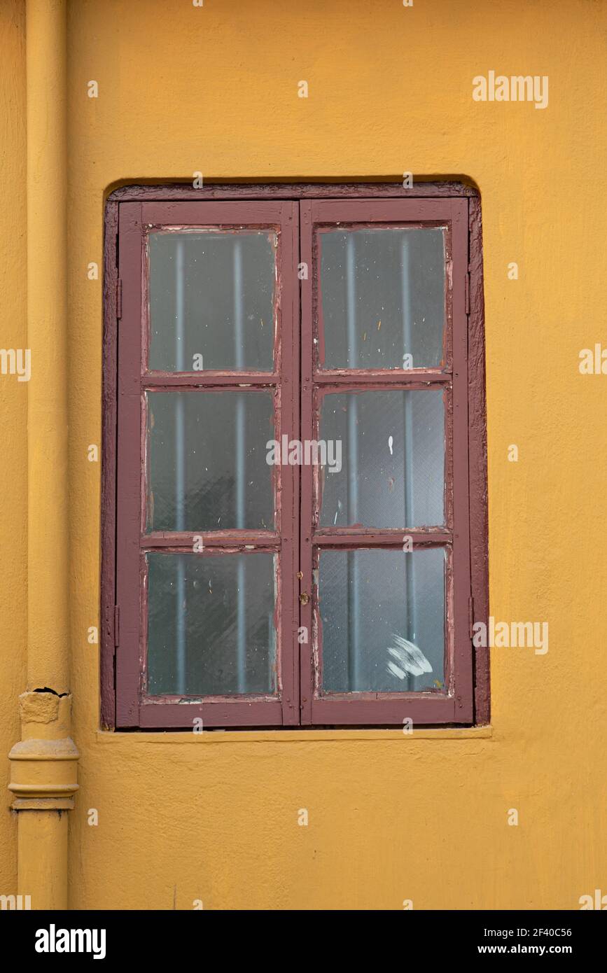 Un cliché vertical d'une vieille fenêtre avec des grilles, des taches et des fissures sur un mur de ciment Banque D'Images