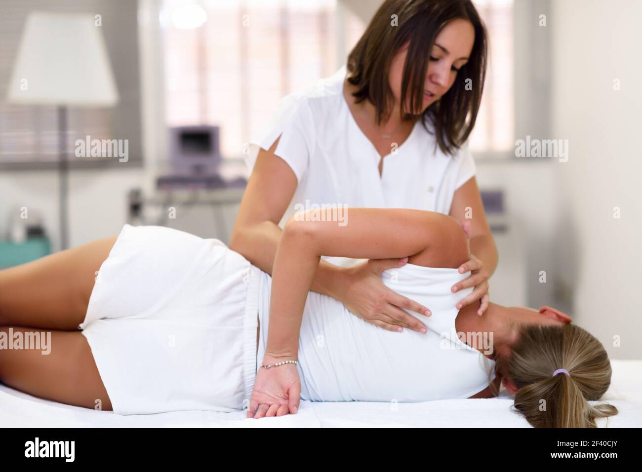 Les professionnels d'un physiothérapeute massage épaule donnant pour femme blonde à l'hôpital. Contrôle médical à l'épaule dans un centre de kinésithérapie. Banque D'Images