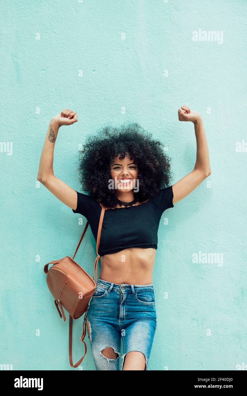 Drôle avec femme noire afro hair raising arms à l'extérieur. Femme portant des vêtements décontractés en contexte urbain. Concept de vie Banque D'Images