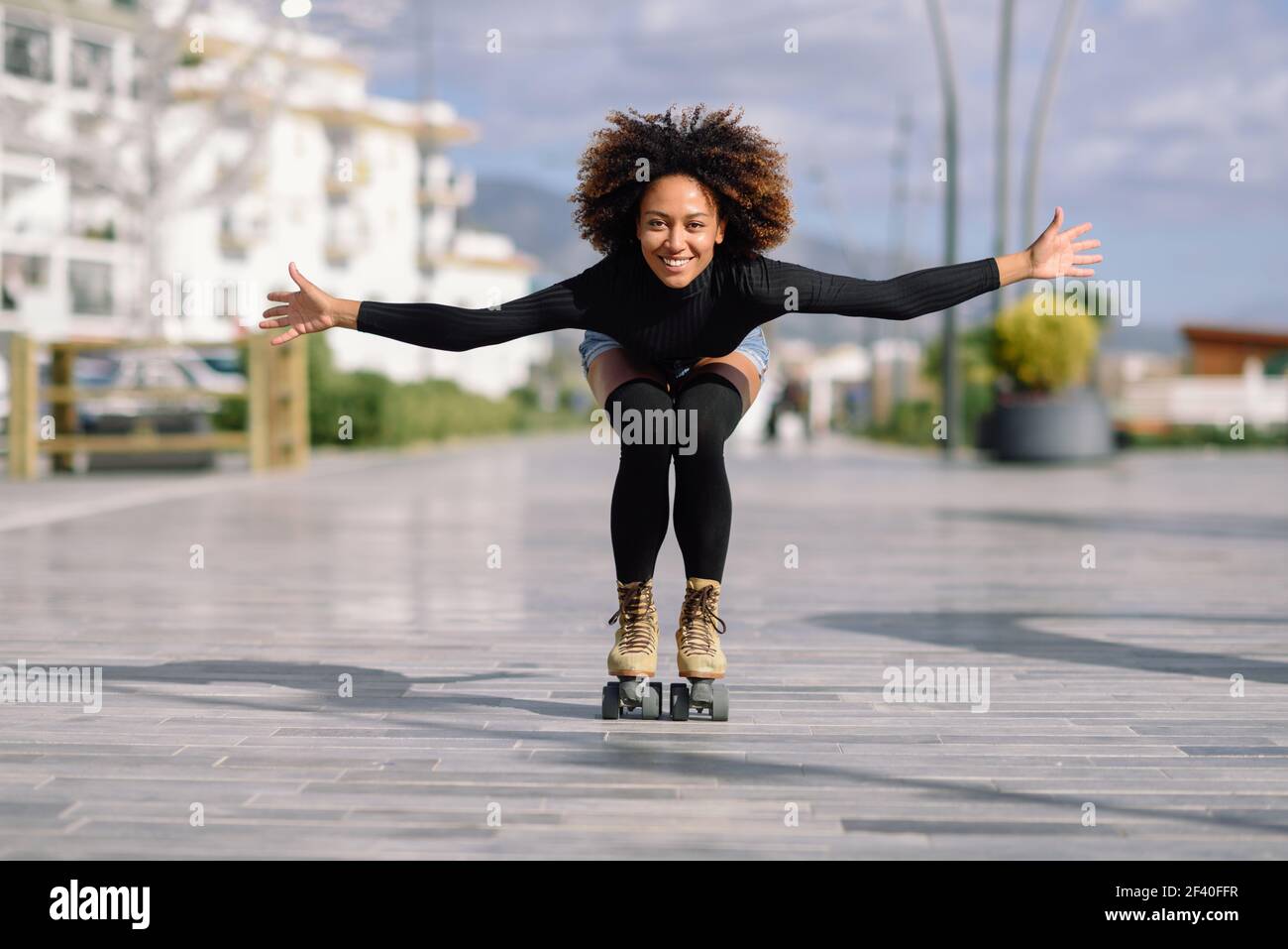 Jeune femme noire monter à cheval sur patins à l'extérieur sur la rue urbain à bras ouverts. Smiling girl avec coiffure afro à roues alignées sur un jour ensoleillé Banque D'Images