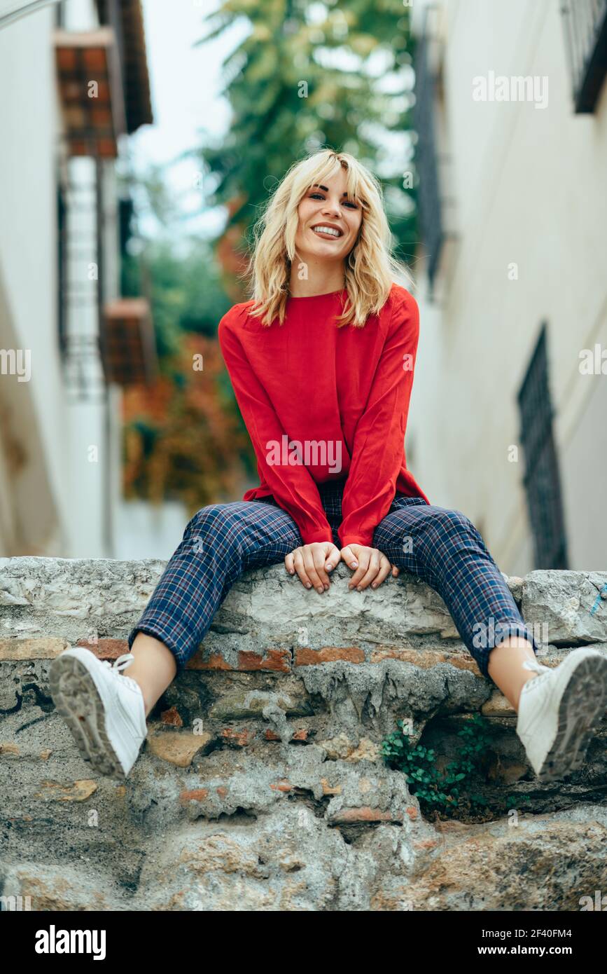 Happy young woman sur fond urbain. Smiling blonde girl with red shirt à profiter de la vie en plein air. Banque D'Images