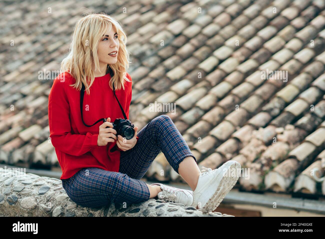 Belle jeune femme blonde prenant des photos avec un ancien appareil photo reflex dans une belle ville. Blonde heureuse femme assise sur des marches urbaines. Jeune femme prenant des photos avec un vieil appareil photo dans une belle ville. Banque D'Images