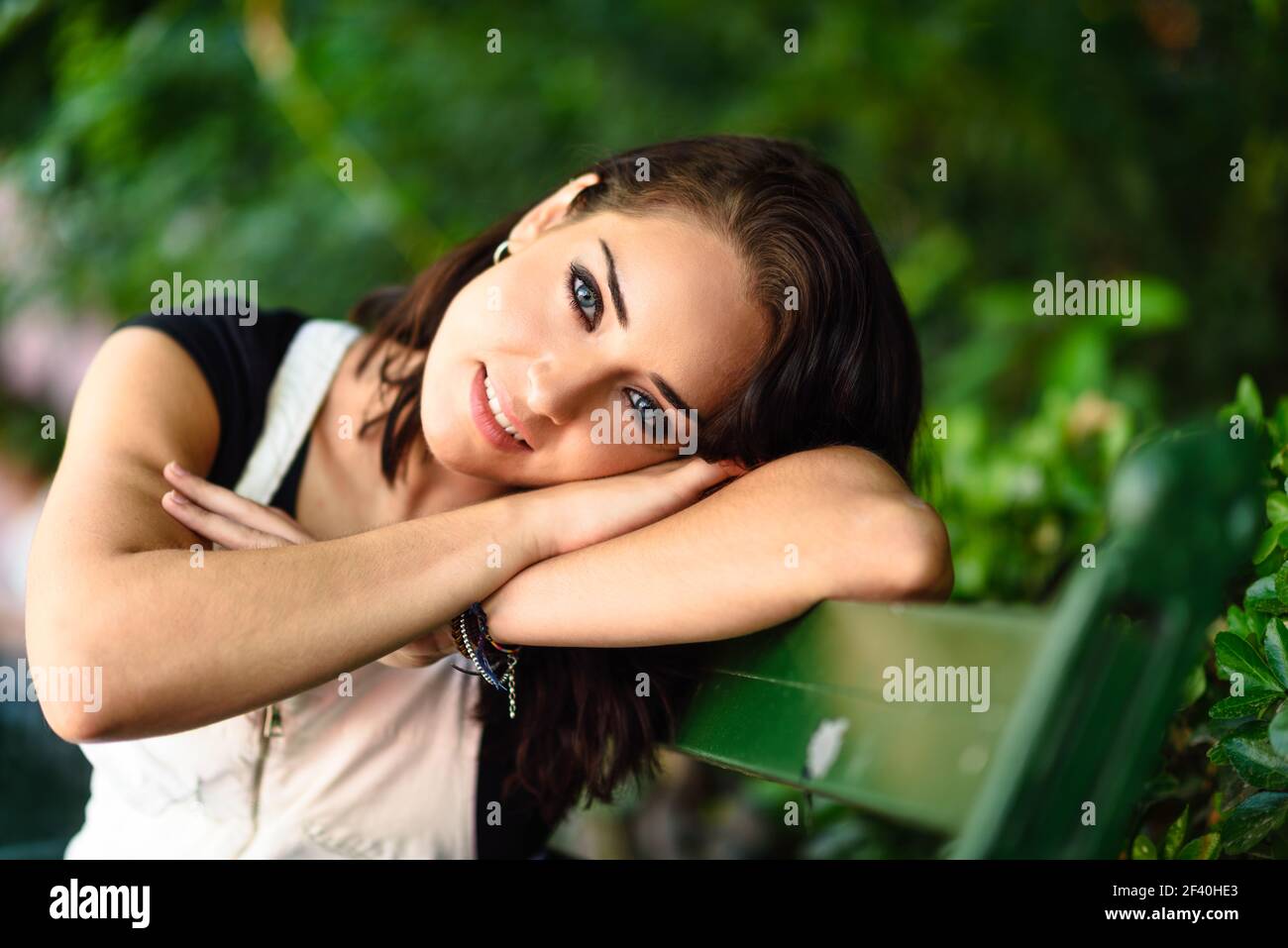 Jeune femme heureuse avec des yeux bleus regardant la caméra assis sur un banc urbain. Belle fille souriante avec un look doux. Jeune femme heureuse avec des yeux bleus regardant la caméra Banque D'Images