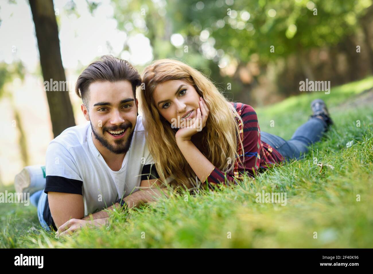 Beau jeune couple allongé sur l'herbe dans un parc urbain. Homme et femme caucasiens portant des vêtements décontractés. Blonde femme. Beau jeune couple allongé sur l'herbe dans un parc urbain. Banque D'Images