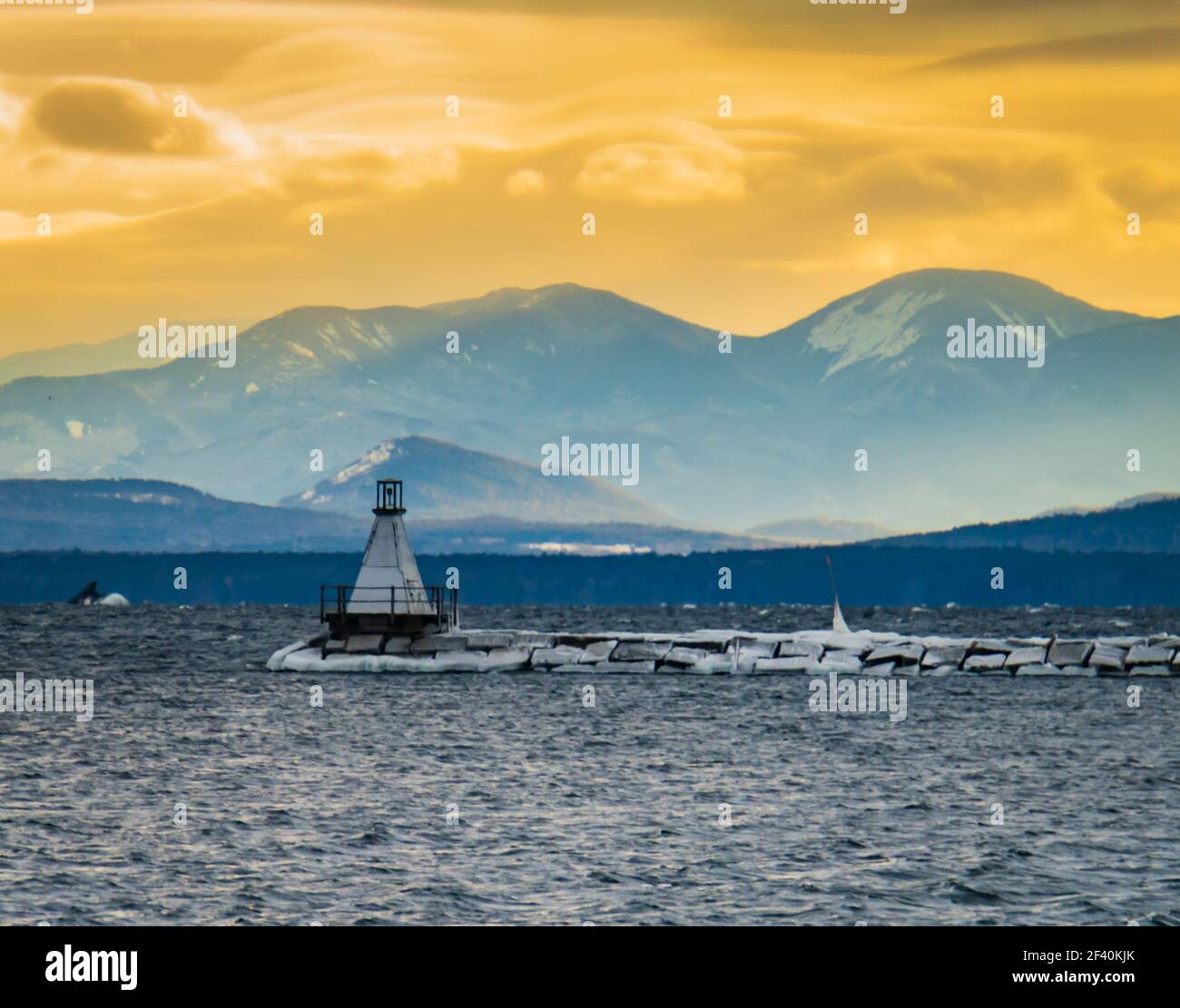 le soleil se dresse sur le phare du brise-lames du lac Champlain avec l'Adirondack Montagnes de New York en face du lac Banque D'Images