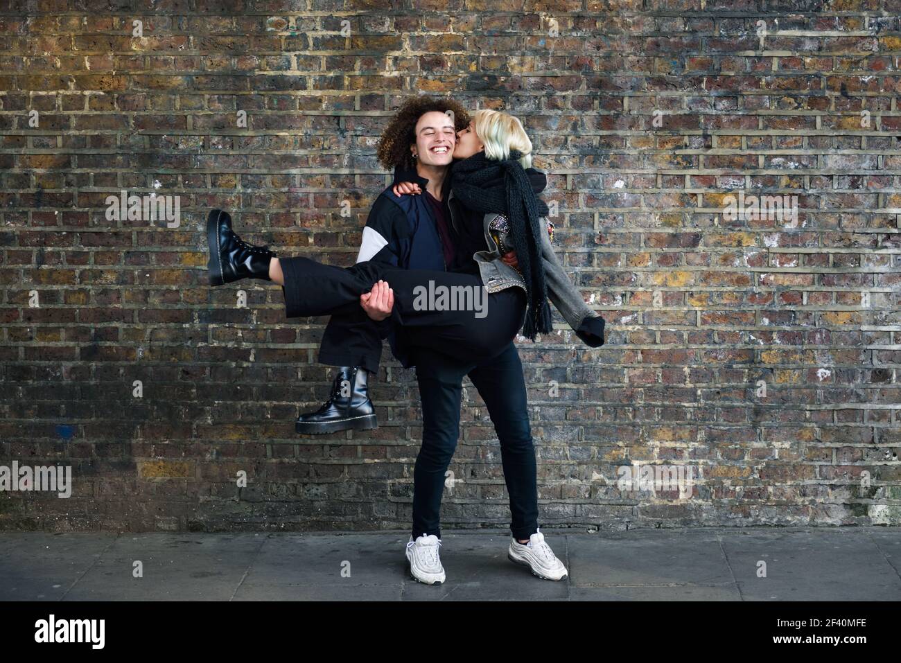 Homme tenant sa petite amie dans ses bras. Jeune couple appréciant la ville de Camden en face d'un mur de briques typique de Londres, Royaume-Uni. Homme tenant sa petite amie dans ses bras devant un mur de briques typique de Londres Banque D'Images