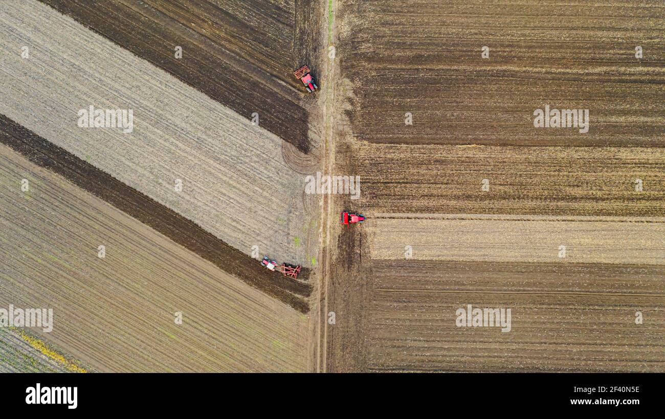 Vue aérienne de dessus de trois tracteurs, l'un traînant une herse à disque et l'autre un cultivateur de semis, le troisième tirant la machine de semoir sur le fie arable Banque D'Images