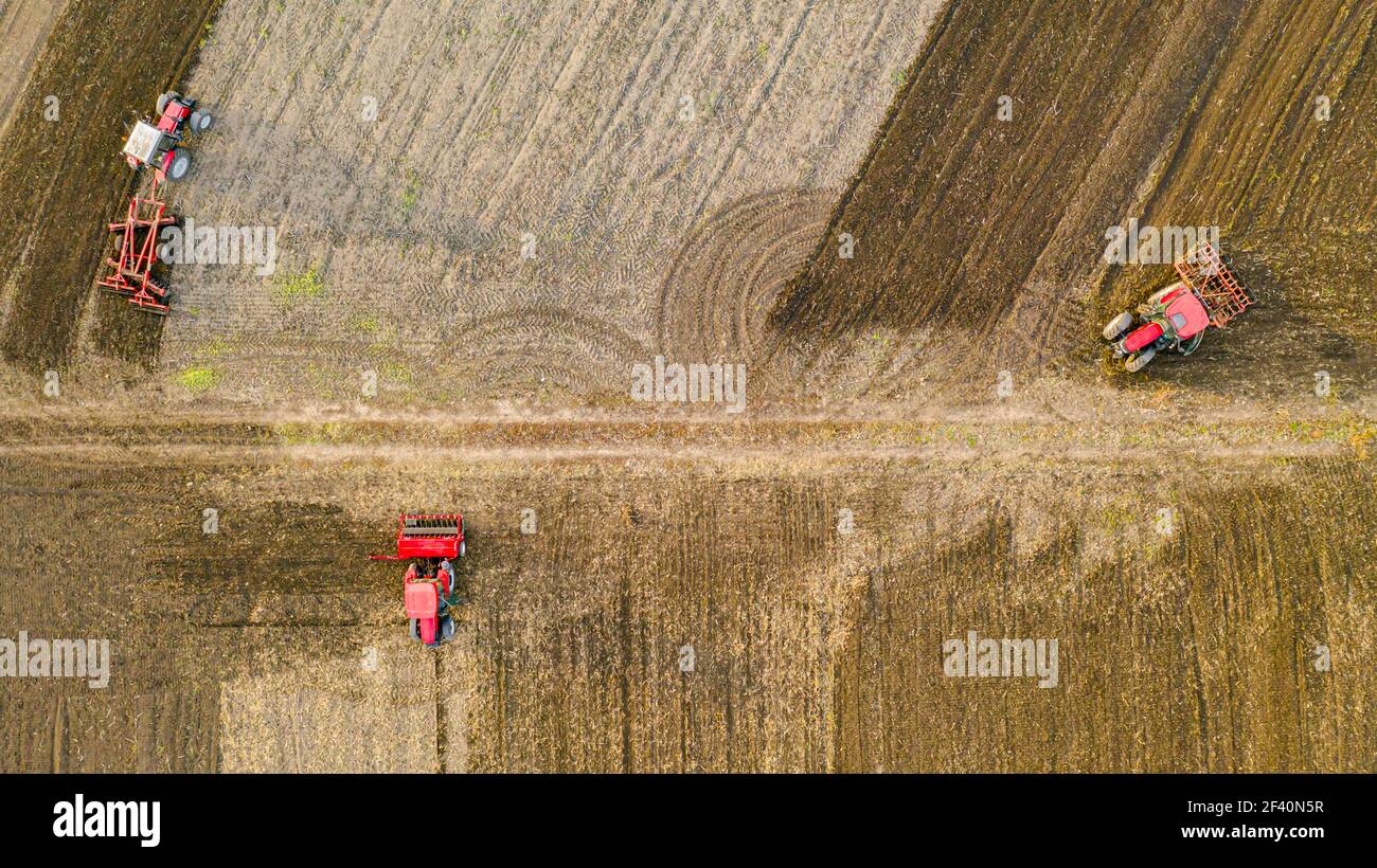 Vue aérienne de dessus de trois tracteurs, l'un traînant une herse à disque et l'autre un cultivateur de semis, le troisième tirant la machine de semoir sur le fie arable Banque D'Images