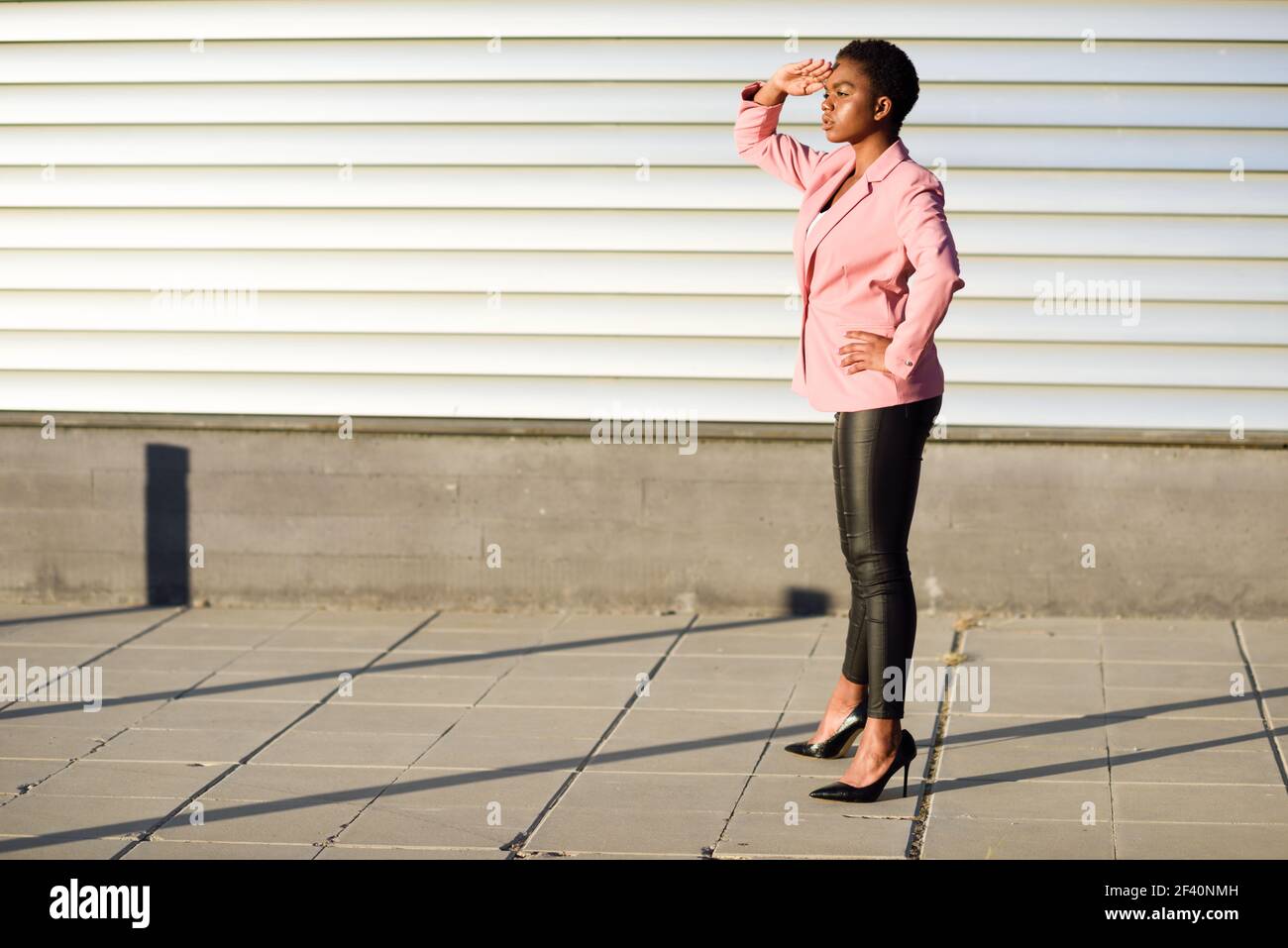 Femme noire, modèle de mode, debout sur un mur urbain. Femme afro-américaine vêtue d'un costume avec veste rose et lumière du coucher du soleil. Femme noire, modèle de mode, debout sur un mur urbain Banque D'Images