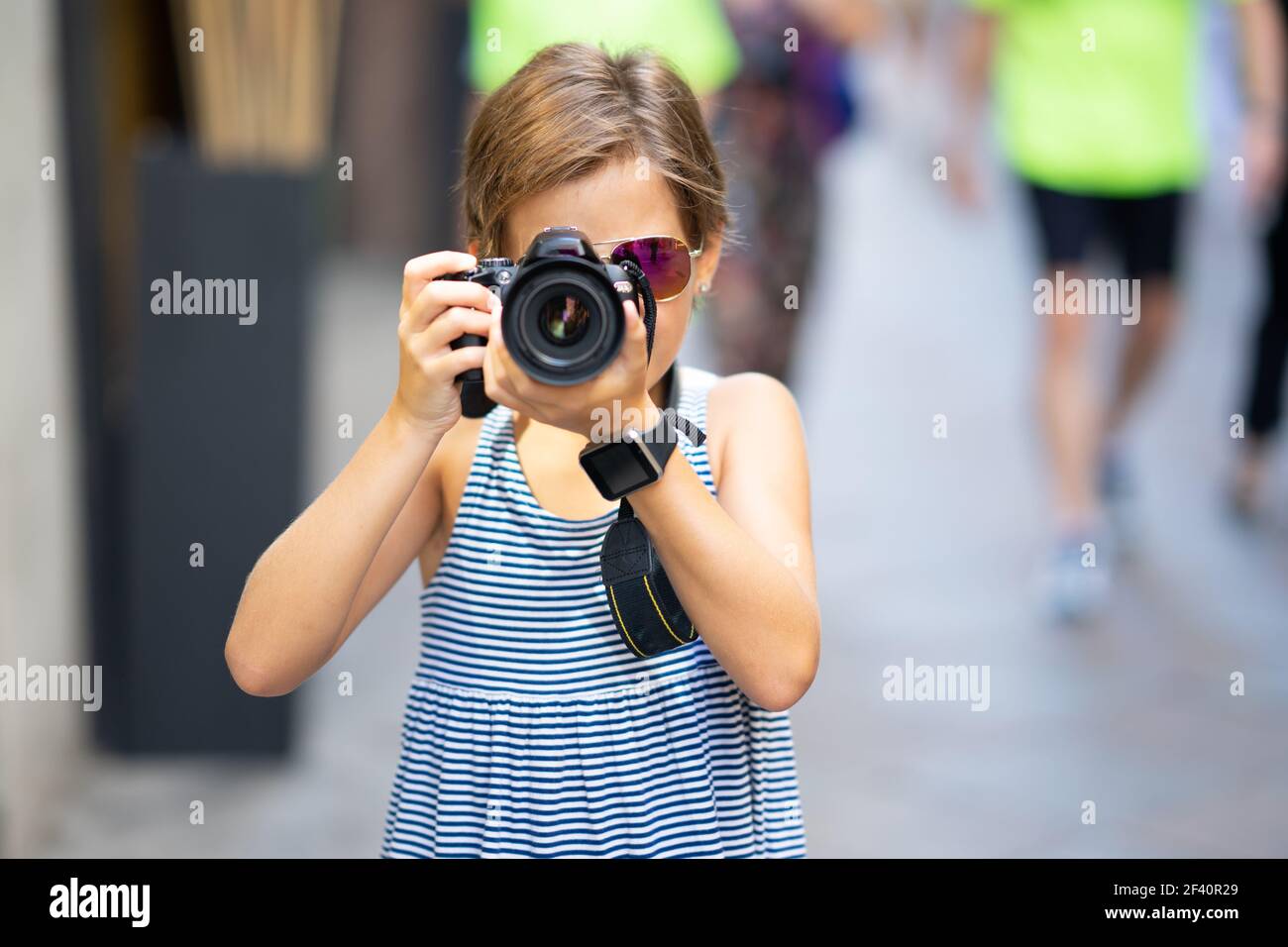 Petite fille qui fait des photos avec un appareil photo reflex numérique dans la rue de la ville. Petite femme voyageant en milieu urbain. Petite fille qui fait des photos avec un appareil photo reflex numérique dans la rue de la ville Banque D'Images