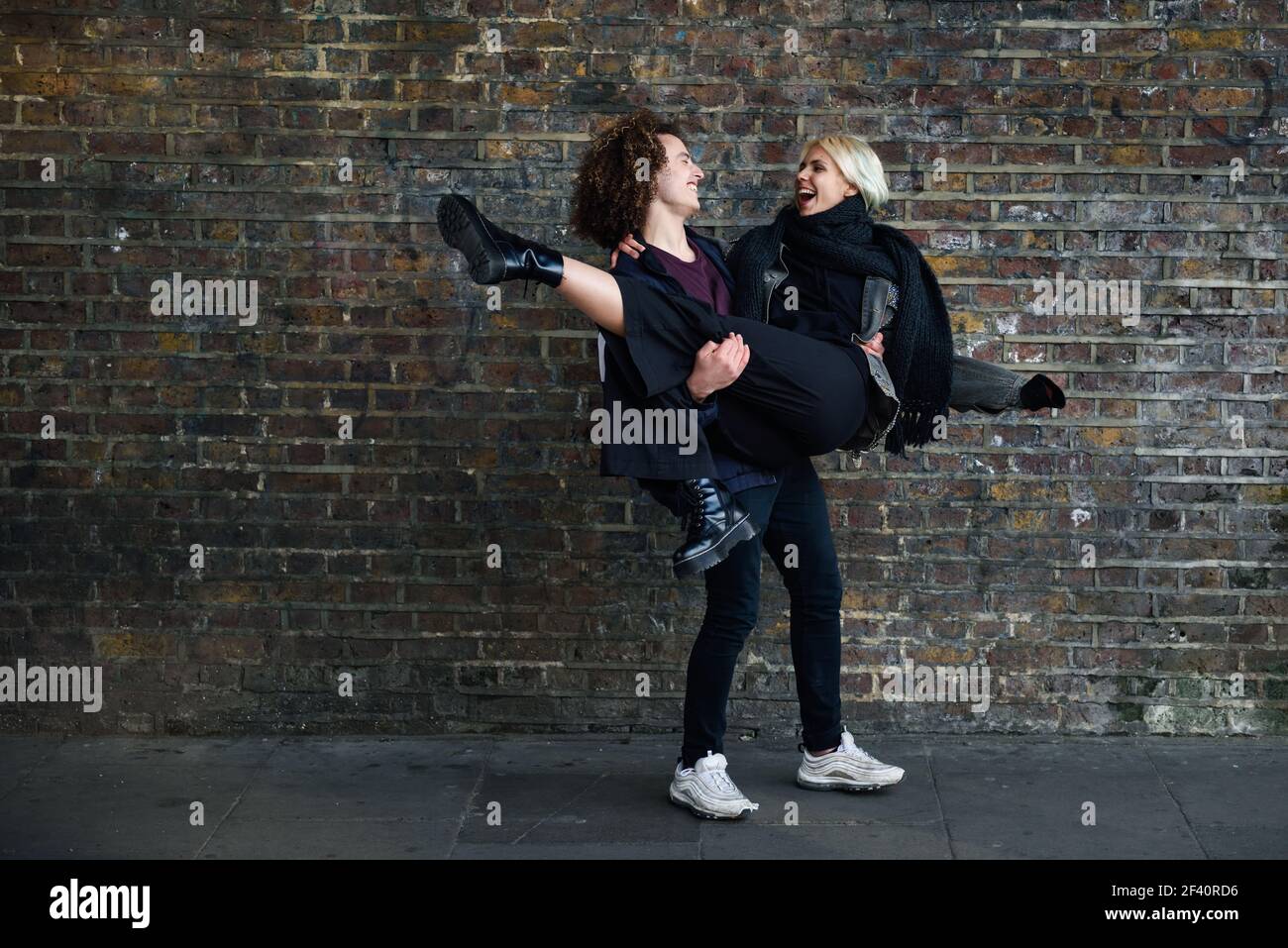 Homme tenant sa petite amie dans ses bras. Jeune couple appréciant la ville de Camden en face d'un mur de briques typique de Londres, Royaume-Uni. Homme tenant sa petite amie dans ses bras devant un mur de briques typique de Londres Banque D'Images