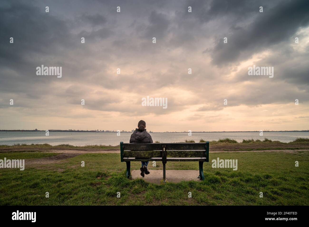 Vue arrière d'une femme assise sur un banc, vue sur la mer, ciel de moody. Banque D'Images