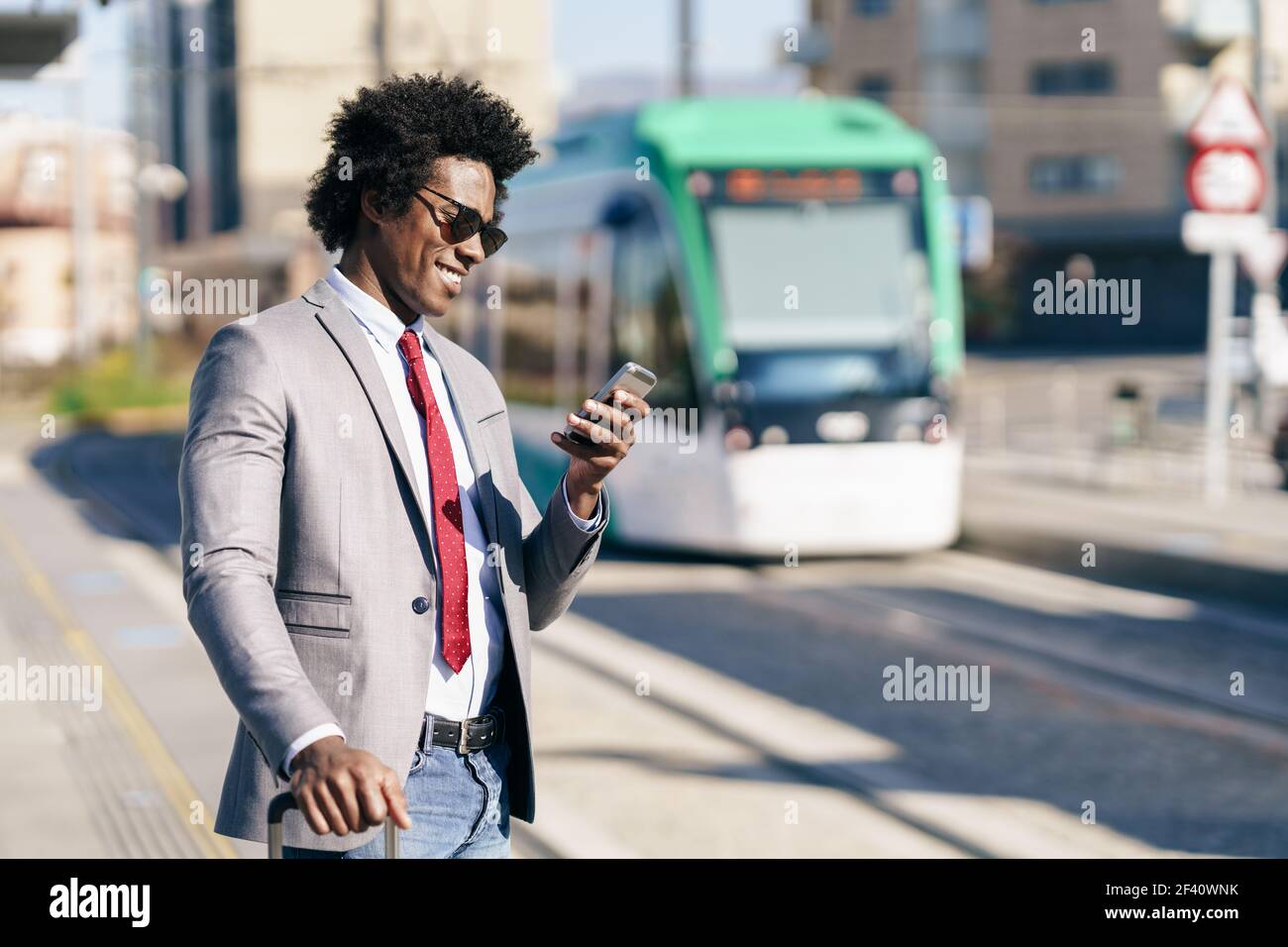 Homme d'affaires noir portant un costume attendant son train sur une gare extérieure. Homme avec cheveux afro.. Homme d'affaires noir vêtu d'un costume qui attend son train Banque D'Images