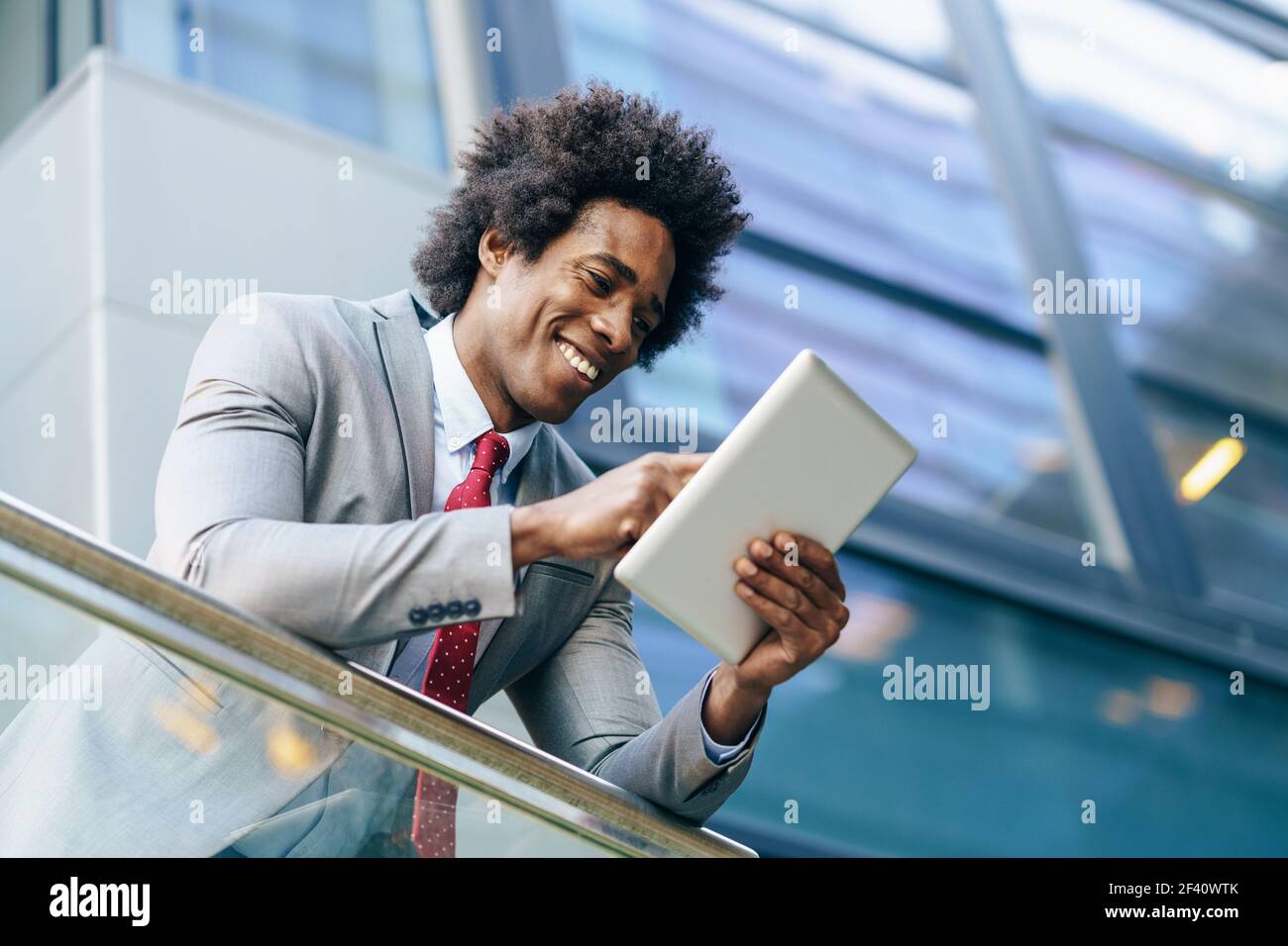 Homme d'affaires noir utilisant une tablette numérique assis près d'un immeuble de bureaux. Homme avec cheveux afro.. Homme d'affaires noir utilisant une tablette numérique assis près d'un immeuble de bureaux. Banque D'Images