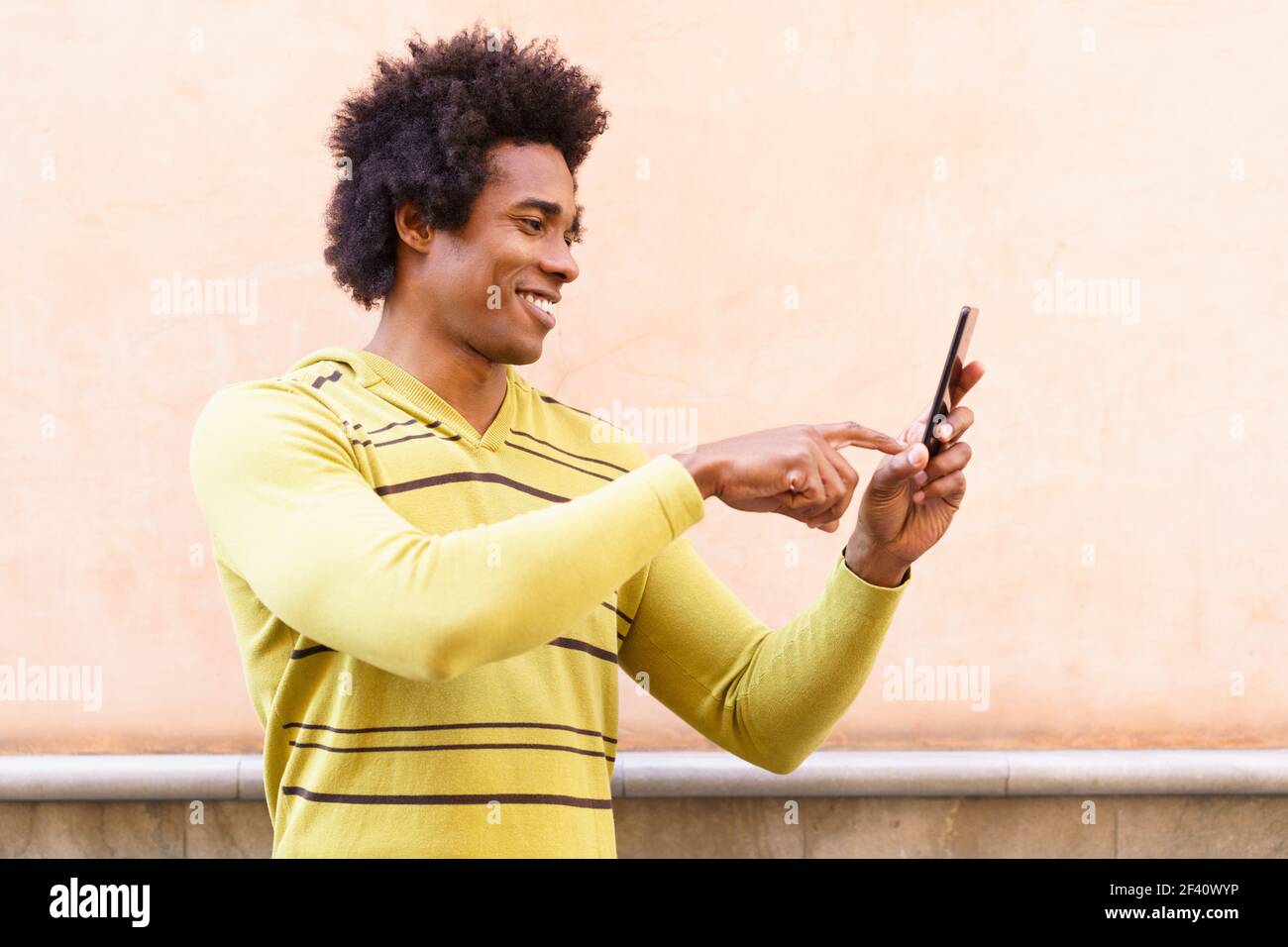 Homme noir avec cheveux afro et casque utilisant un smartphone en milieu urbain. Homme noir avec cheveux afro et casque à l'aide d'un smartphone. Banque D'Images