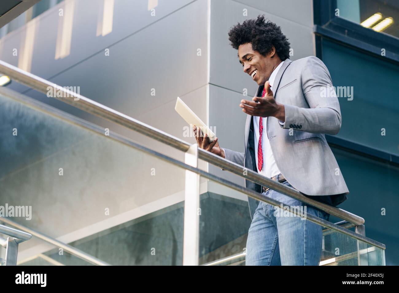 Homme d'affaires noir utilisant une tablette numérique assis près d'un immeuble de bureaux. Homme avec cheveux afro.. Homme d'affaires noir utilisant une tablette numérique assis près d'un immeuble de bureaux. Banque D'Images