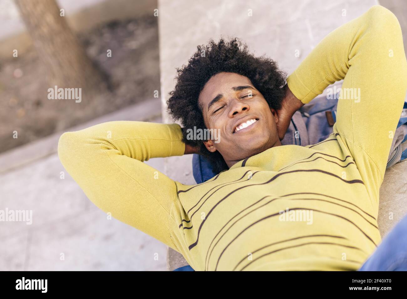 Touriste noir cubain avec des cheveux afro couchés sur le sol, sur son sac à dos, se reposant de son voyage à Grenade, Andalousie, Espagne. Touriste noir avec des cheveux afro couchés au sol à l'extérieur. Banque D'Images