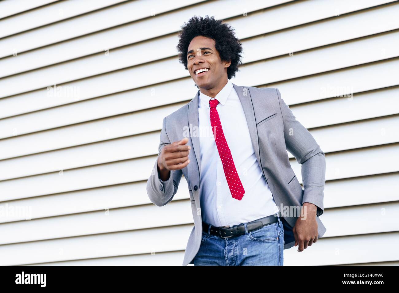 Joyeux homme d'affaires noir vêtu d'un costume dansant à l'extérieur. Homme avec cheveux afro.. Joyeux homme d'affaires noir vêtu d'un costume dansant à l'extérieur. Banque D'Images