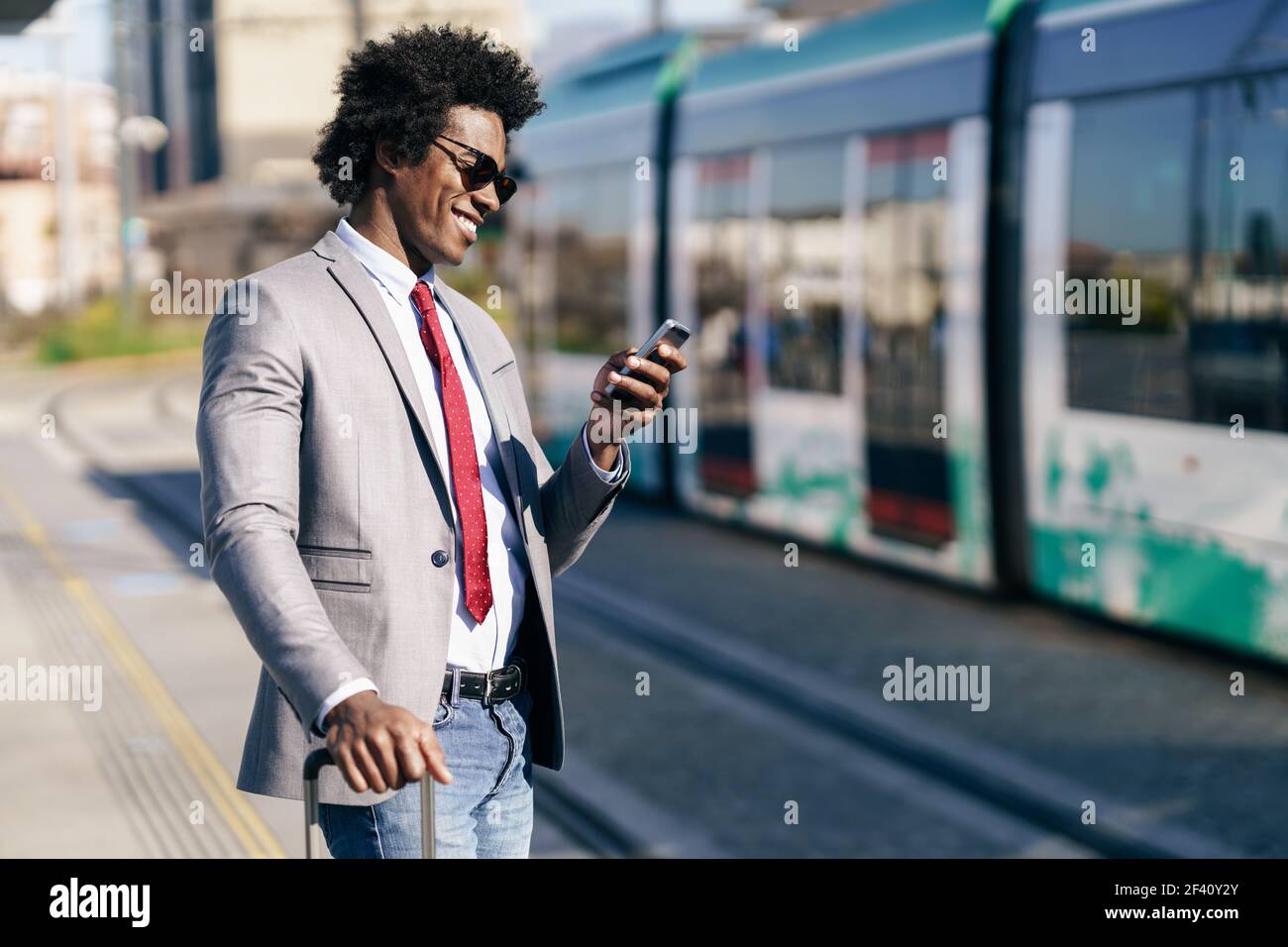 Homme d'affaires noir souriant attendant le prochain train. Homme avec des cheveux afro navettage.. Homme d'affaires noir souriant attendant le prochain train Banque D'Images