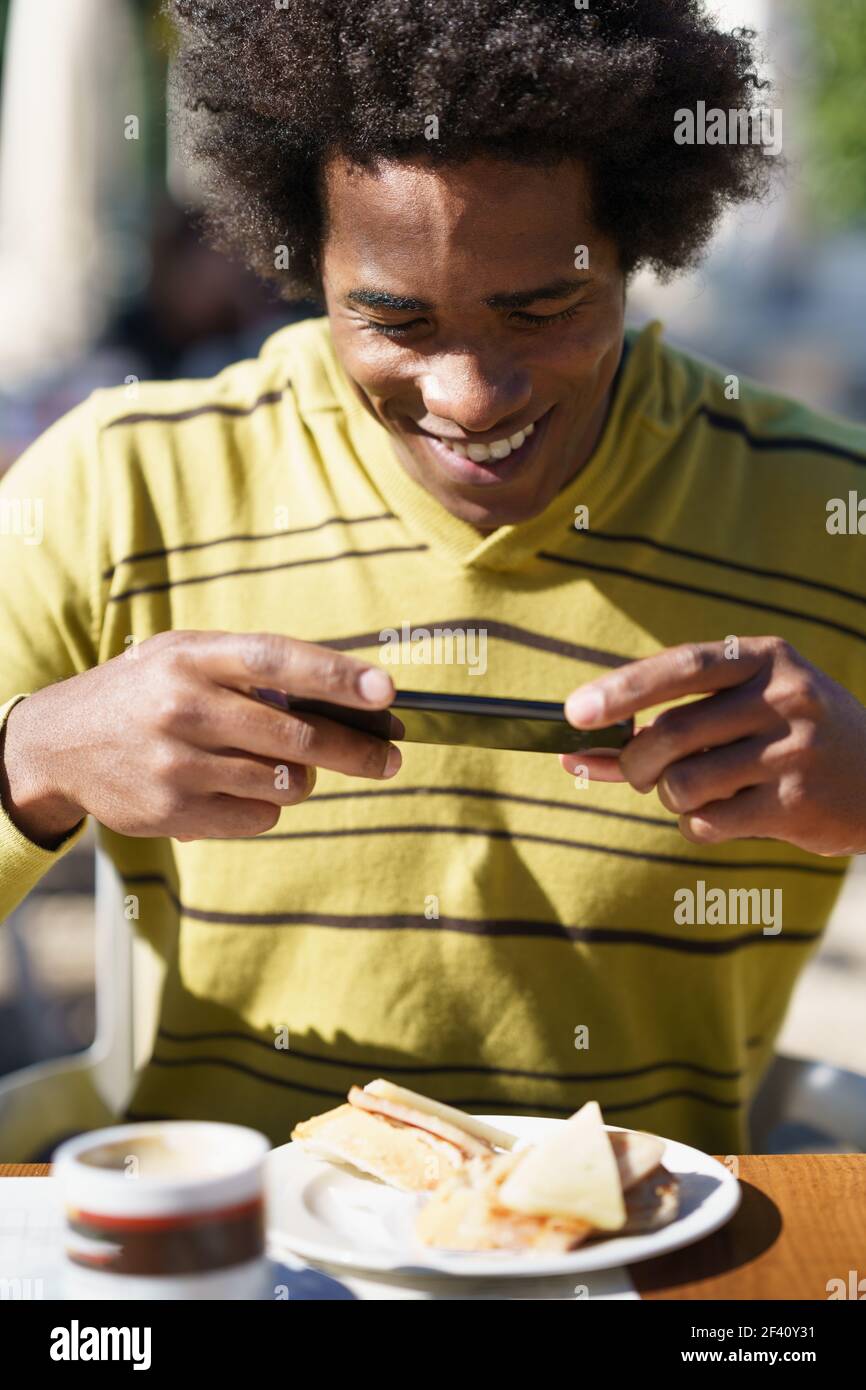 Cuban Black prendre une photo avec son smartphone à un snack dans un bar assis à la table à l'extérieur lors de son voyage à Grenade, Espagne. Cuban Black prendre une photo avec son smartphone à un snack Banque D'Images