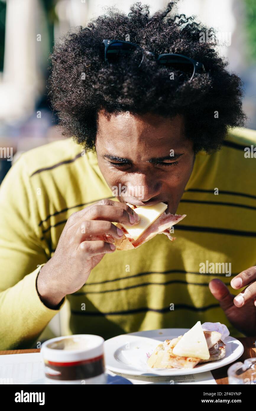 Homme noir cubain ayant un snack dans un bar assis à la table à l'extérieur lors de son voyage à Grenade, Espagne. Homme noir ayant un snack dans un bar assis à la table à l'extérieur Banque D'Images