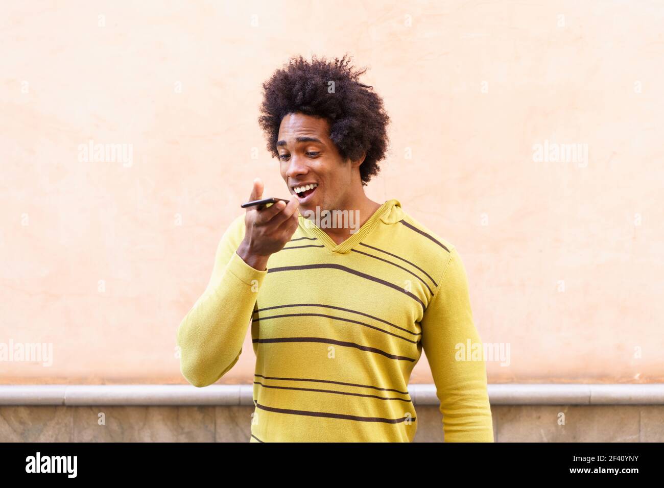 Homme noir avec cheveux afro et casque à l'aide d'un smartphone envoyant une note vocale. Homme noir avec cheveux afro et casque à l'aide d'un smartphone. Banque D'Images