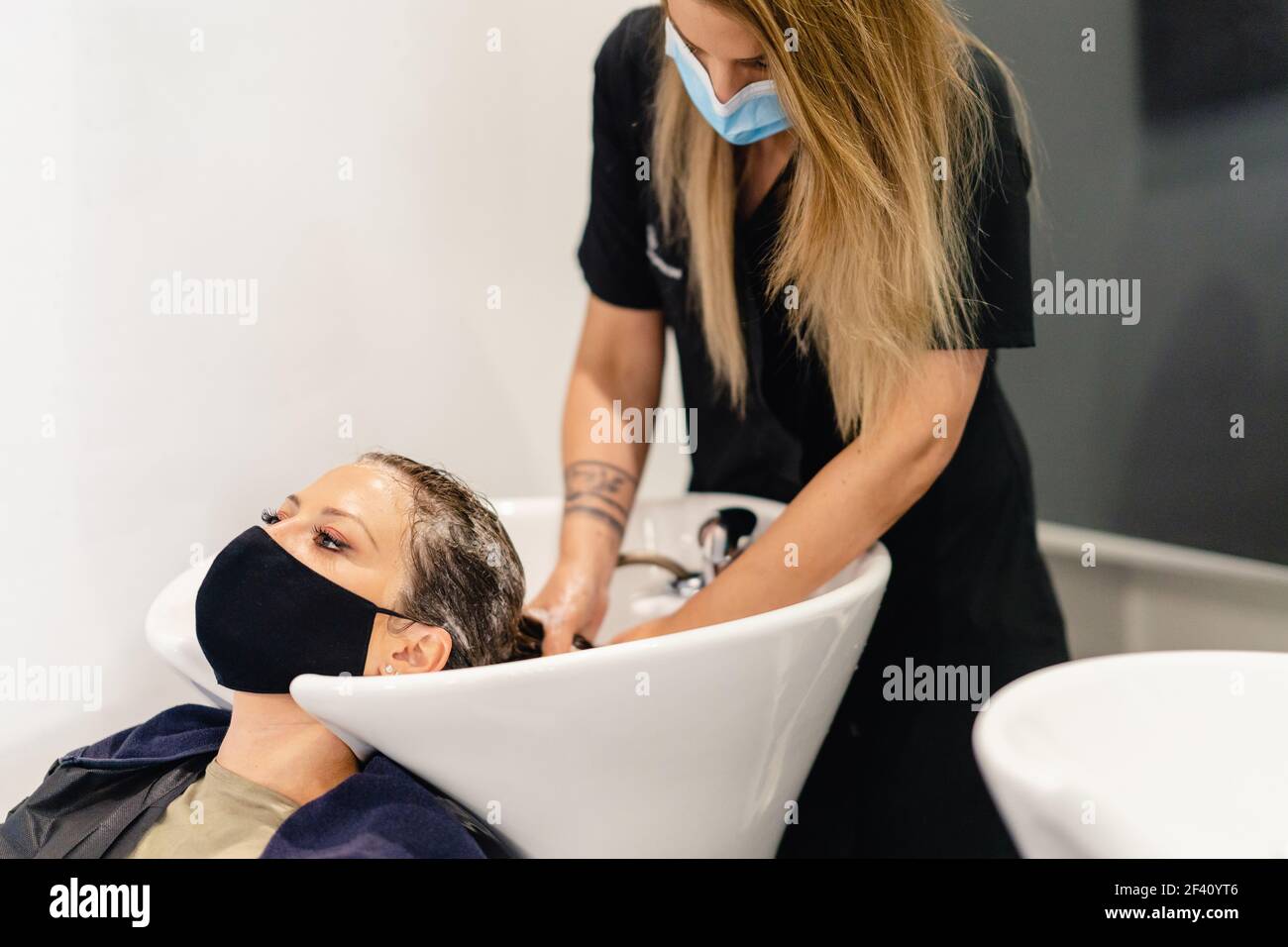 Femme coiffeur lavant la tête d'un client dans un salon, protégée par un masque contre Covid-19. Femme coiffeur lavant la tête d'un client dans un salon, protégé par un masque Banque D'Images