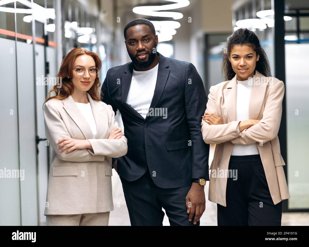 Les partenaires d'affaires influents regardent la caméra en toute confiance, souriant. Les collègues multiraciaux qui réussissent dans un vêtement élégant et formel sont debout dans un concept moderne de bureau, de travail d'équipe Banque D'Images