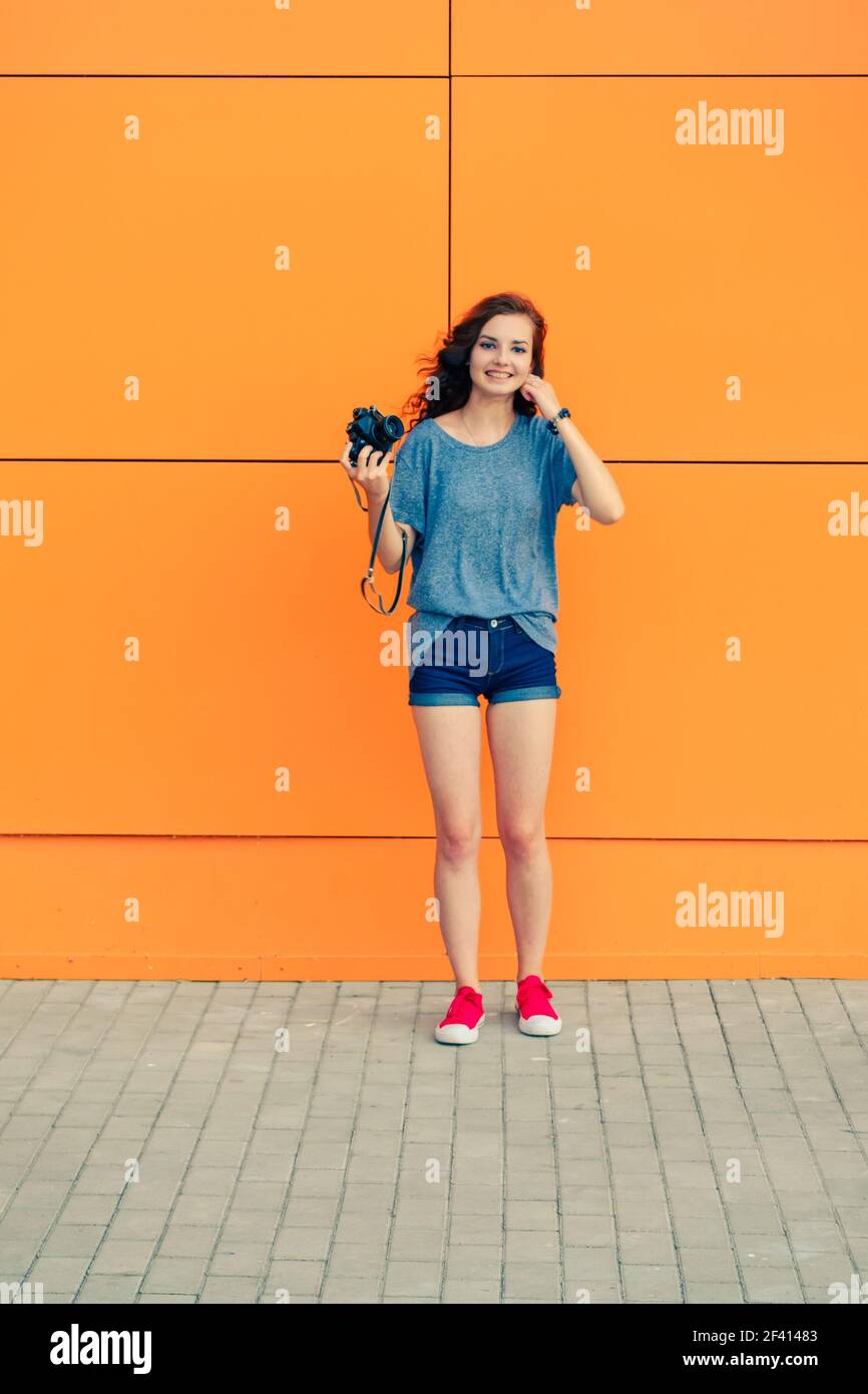 Bonne fille avec un appareil photo rétro dans ses mains debout devant le mur orange. Bonne fille avec un appareil photo rétro dans ses mains Banque D'Images