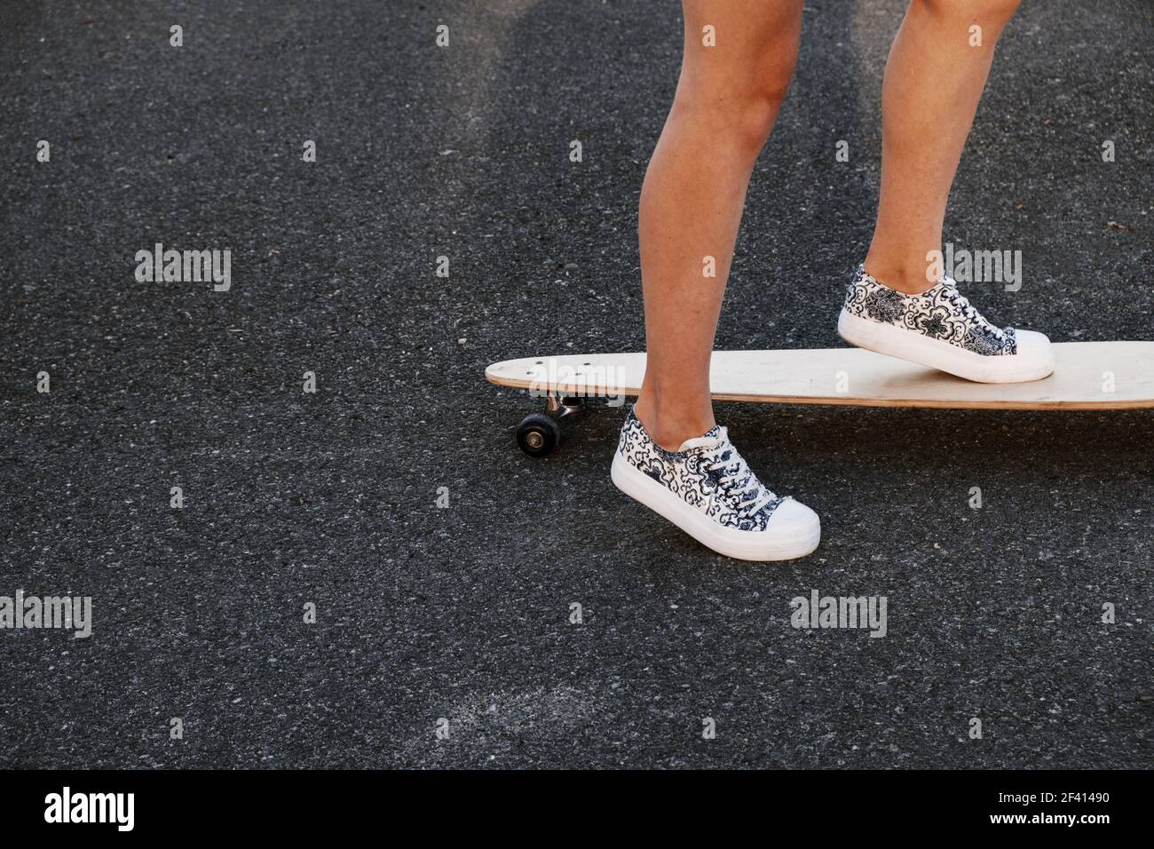 Fille prête à pousser son skate vers l'avant. Gros plan des pieds de skateboarder de fille tout en patinant dans le parc sur la surface d'asphalte, tourné avec beaucoup d'espace de copie. Gros plan des pieds de skate de fille tout en patinant dans le parc sur la surface d'asphalte Banque D'Images