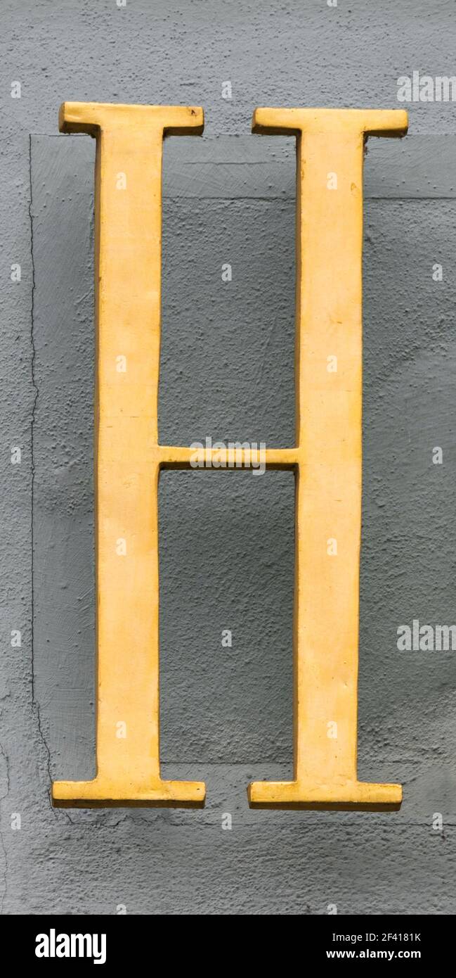 Lettre d'or H flottant devant le mur gris de la maison Banque D'Images