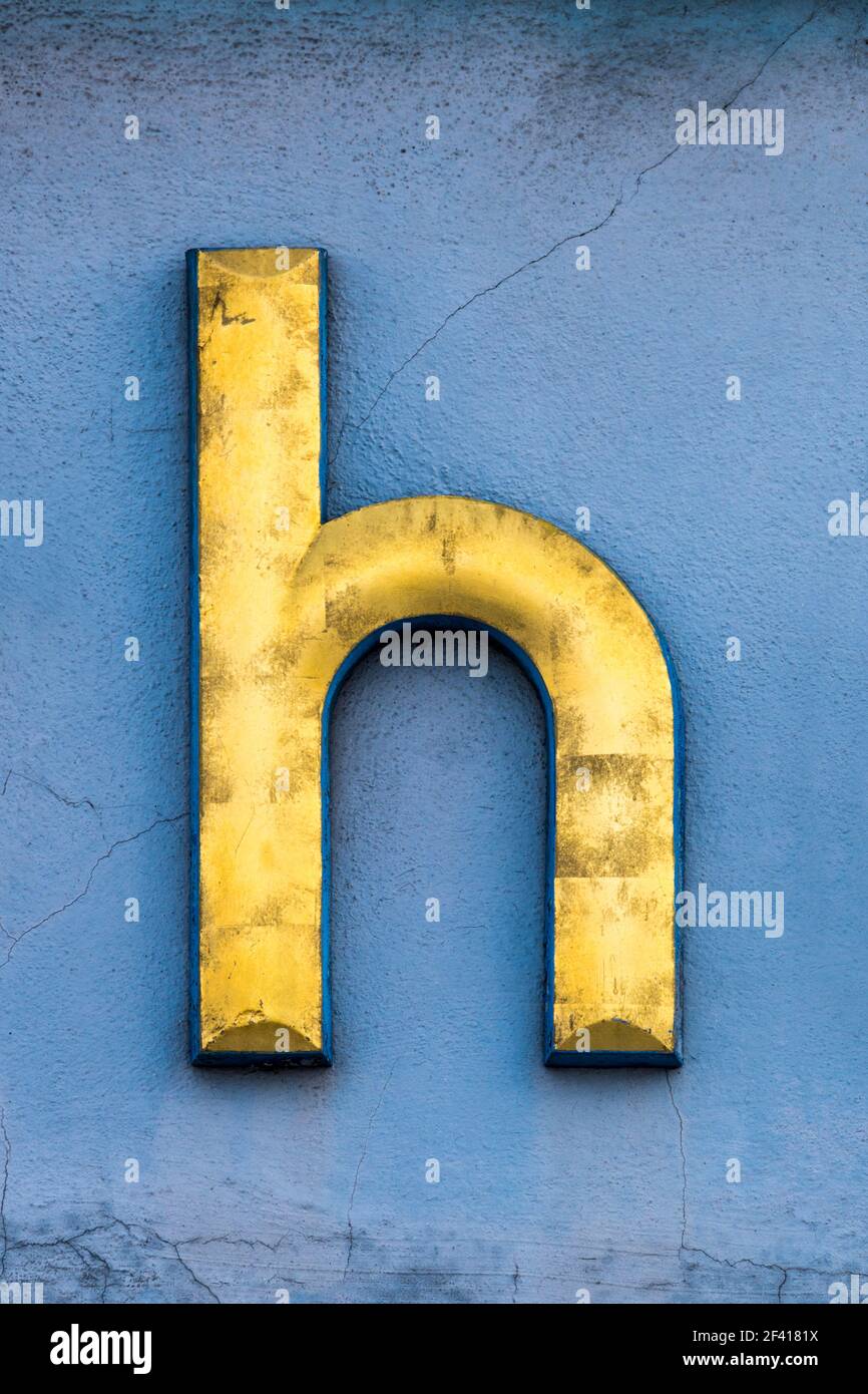Lettre d'or h sur un mur bleu Banque D'Images