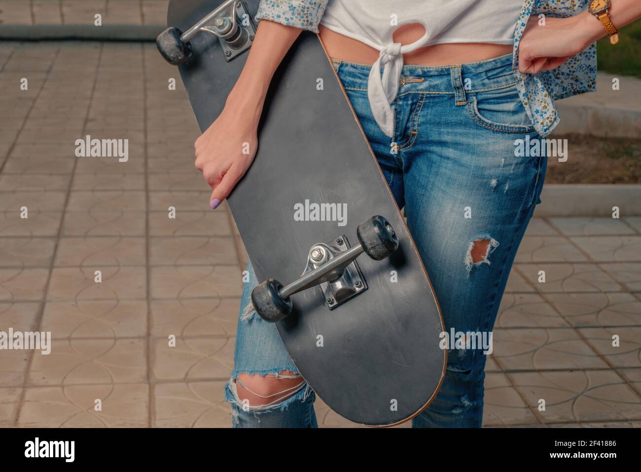 Fille tenant le skateboard devant son corps tourné avec le copyspace. Fille tenant une planche à roulettes devant son corps Banque D'Images