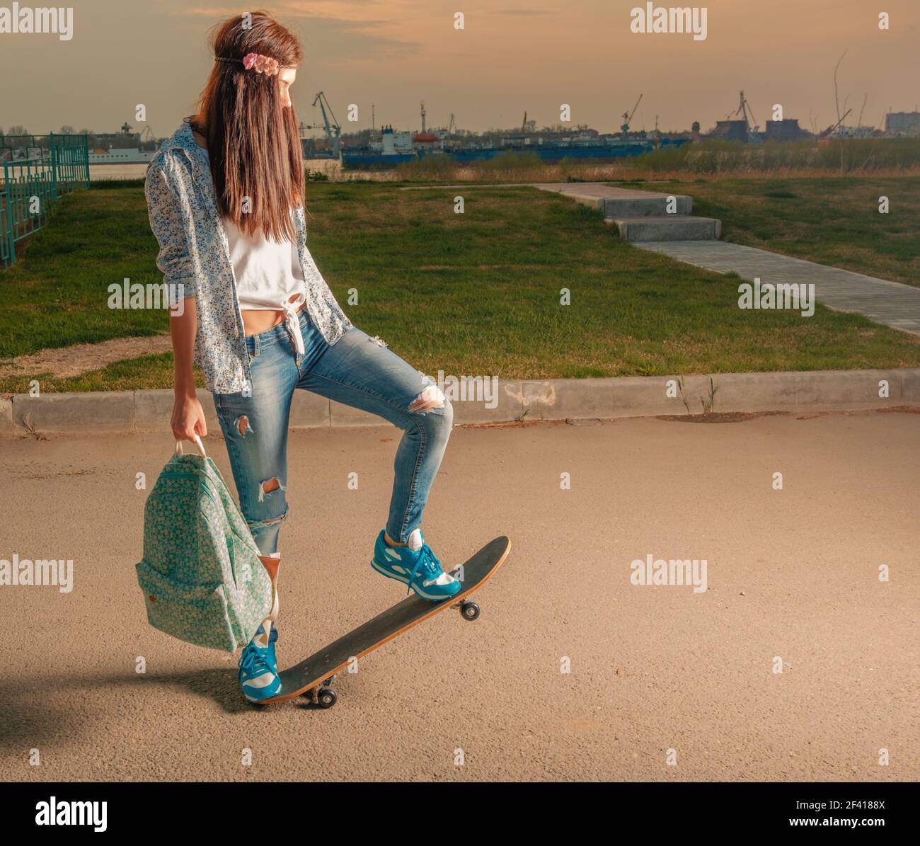 Petite fille sur un skateboard avec un sac à dos dans ses mains. Petite fille sur planche à roulettes avec sac à dos Banque D'Images
