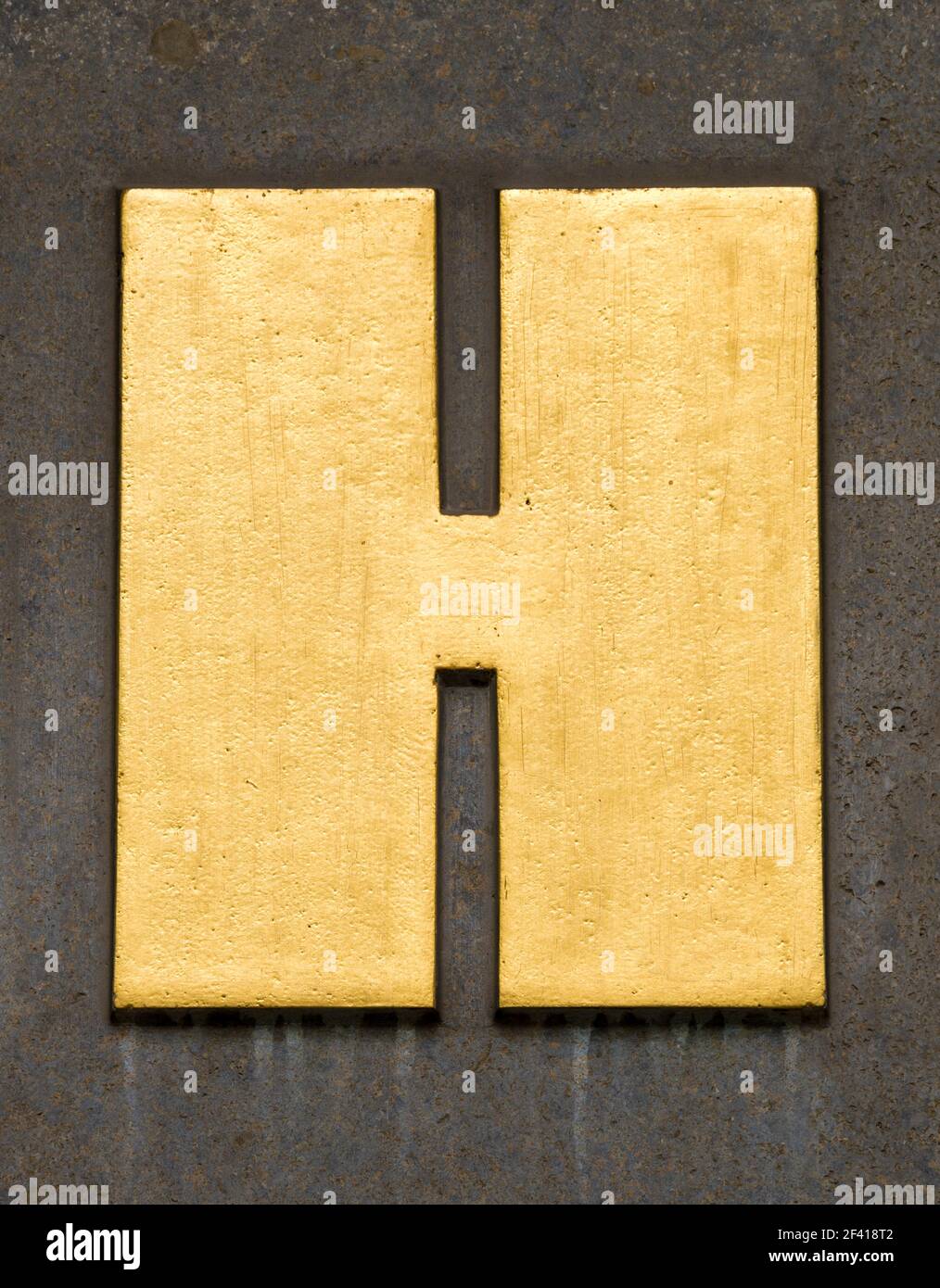 Lettre d'or H sur un mur brun Banque D'Images