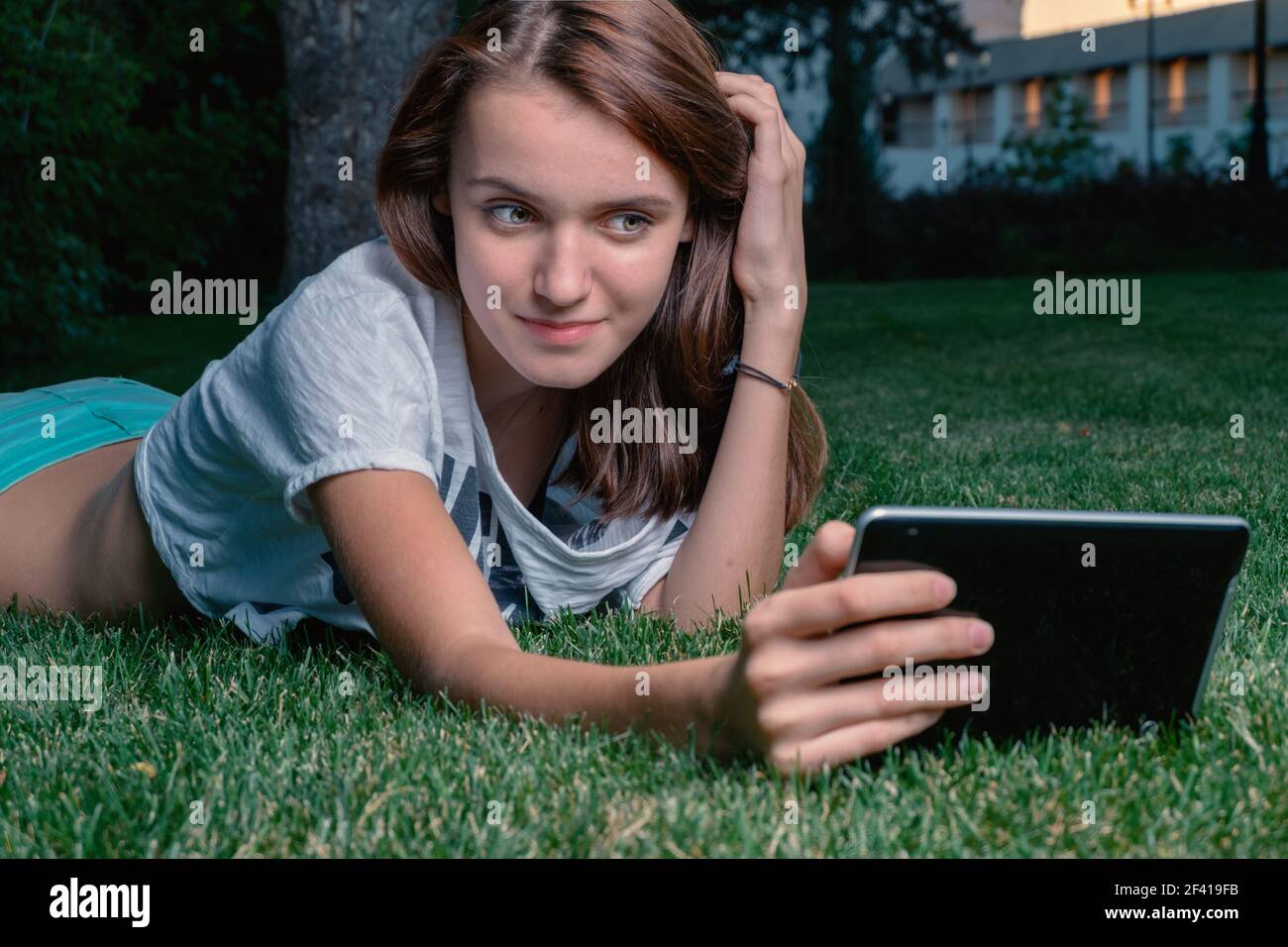 Jeune fille tablette utilisateur d'ordinateur couché sur l'herbe verte de parc et de lecture des messages. Jeune fille tablette utilisateur d'ordinateur couché le long de l'herbe verte de parc et flirting Banque D'Images