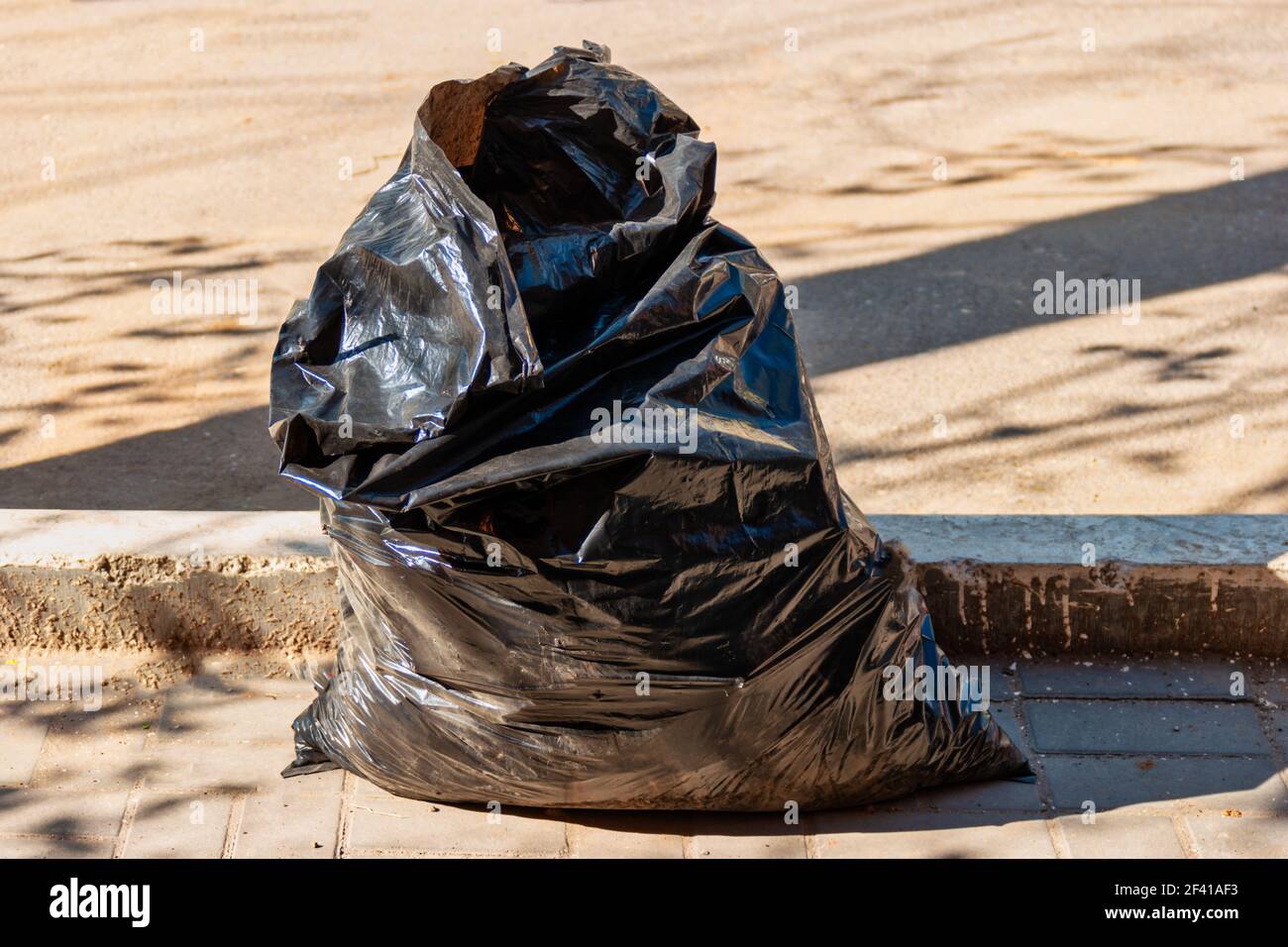 Le sac de punk en plastique noir avec les déchets ménagers est posé sur le sol près du trottoir dans la rue. Sac punk en plastique noir avec déchets ménagers près du trottoir dans la rue Banque D'Images