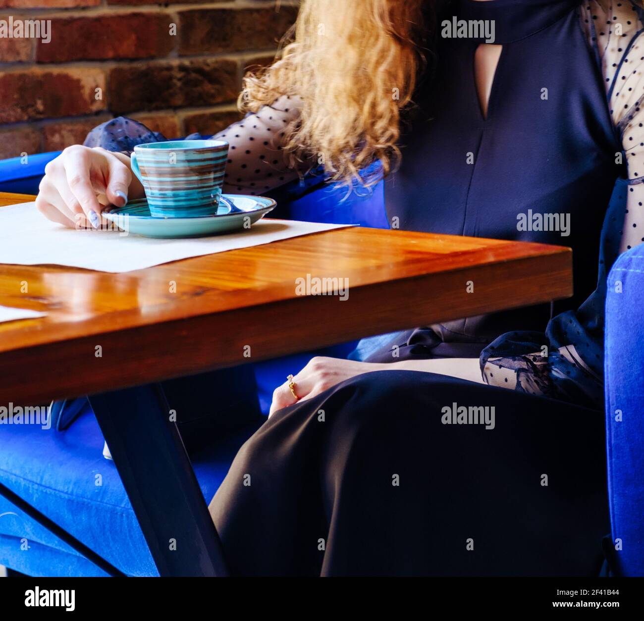 Une jeune femme aux cheveux bruns se repose dans la cafétéria à une table près de la fenêtre. Nous voyons la table elle-même et la tasse tenue par la main de la fille et de la rsquo, son autre main reposant sur ses genoux, et la lumière de la fenêtre tombe sur tout cela. Une jeune femme aux cheveux rouge bouclés se repose dans la cafétéria à une table près de la fenêtre. Nous voyons la table elle-même et la coupe que la fille tient avec sa main, et la lumière de la fenêtre tombe sur tout. Banque D'Images